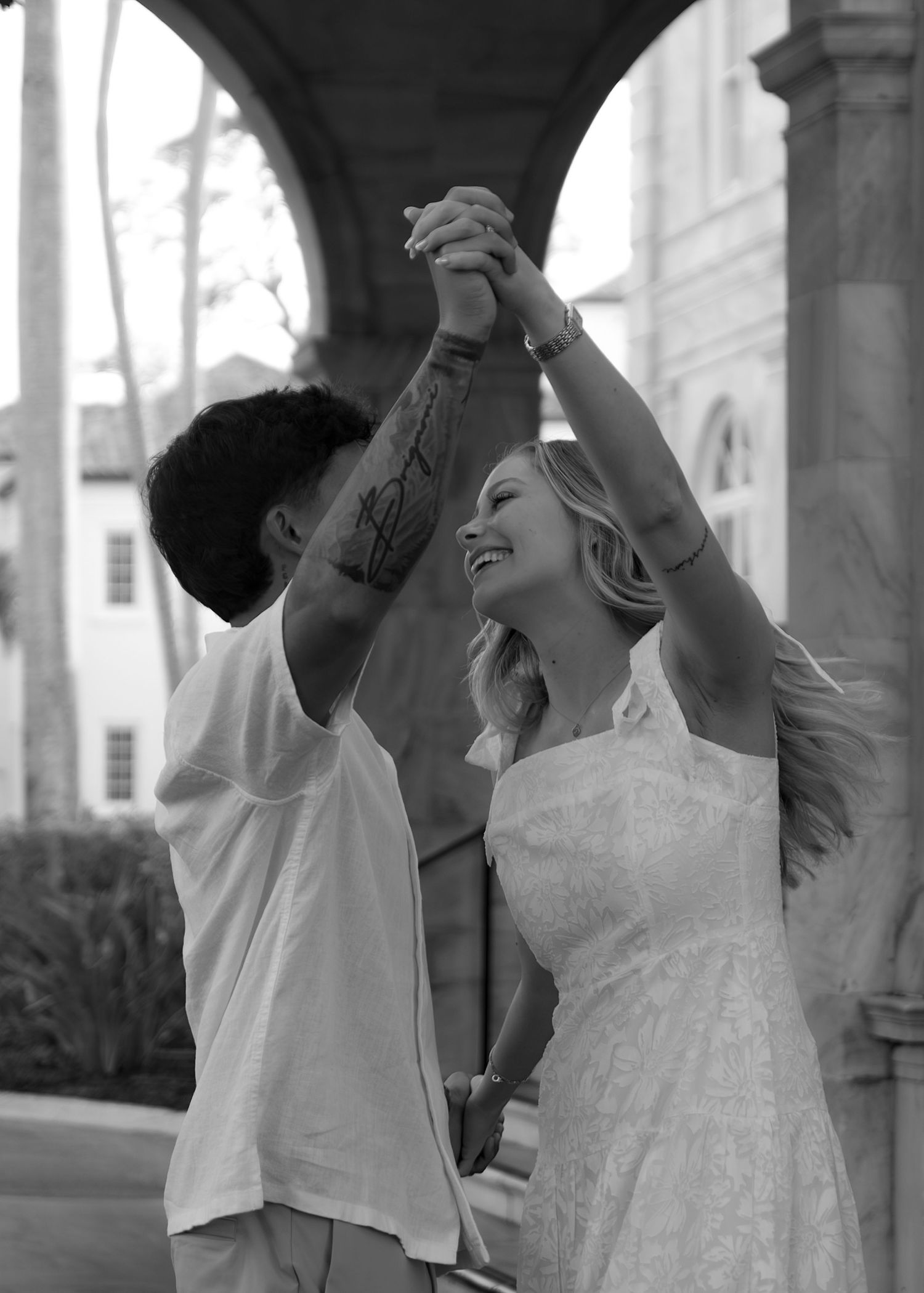 Black and white photo of a smiling couple dancing outdoors near ornate stone arches.