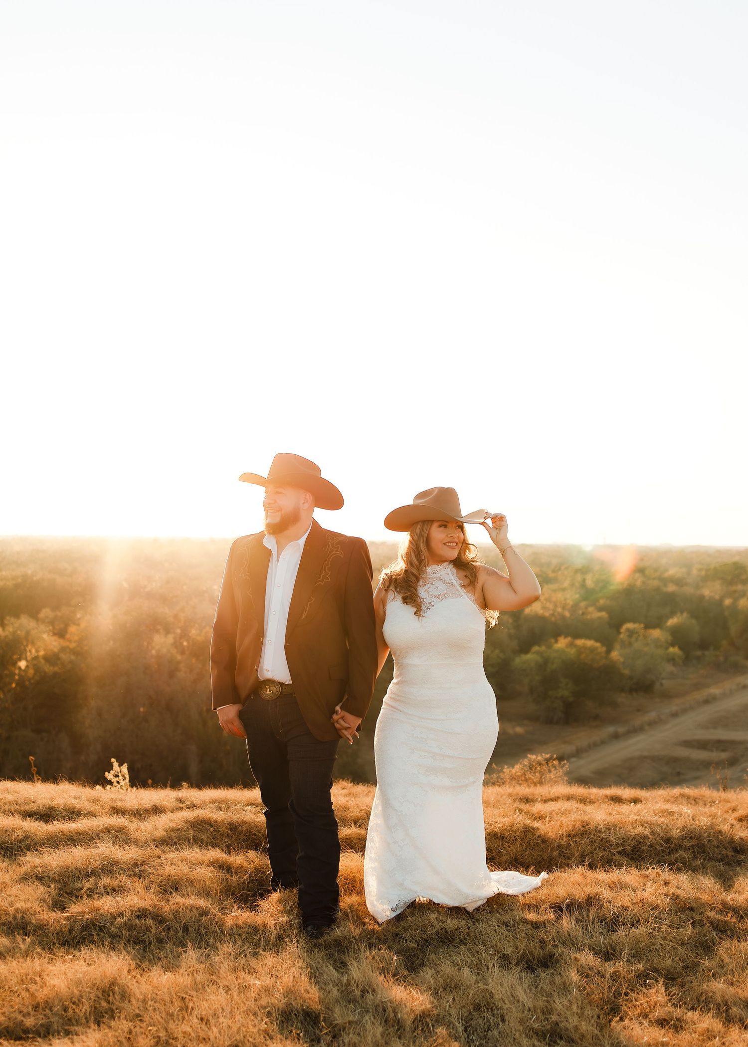 Bride and groom in cowboy hats holding hands at golden sunset on a Texas hill country ranch.
