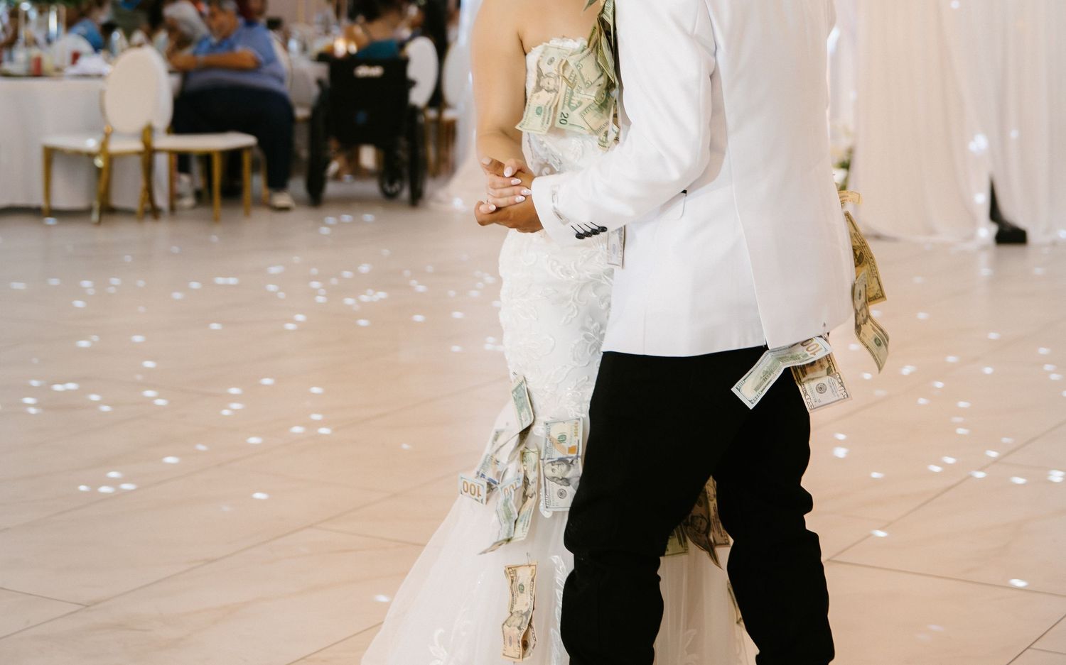 Bride and groom share first dance at wedding reception, bride wearing elegant white gown with floral details.