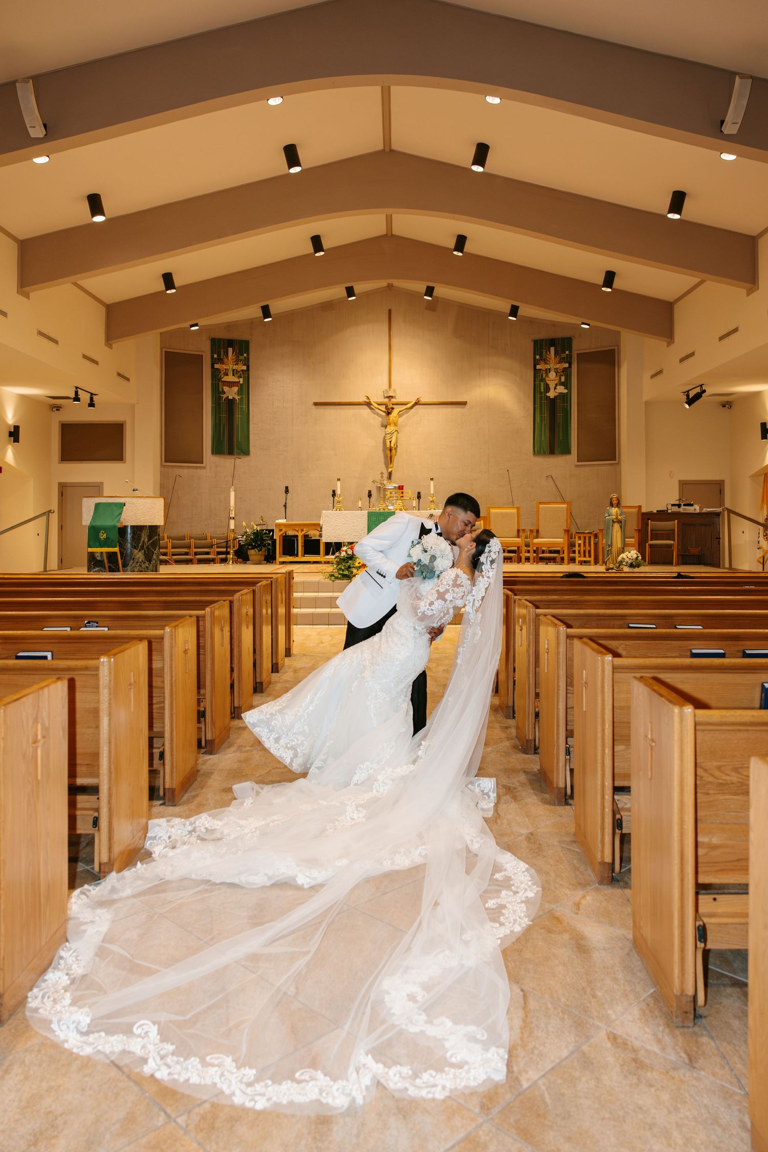 Bride and groom share romantic dip kiss in church aisle after ceremony.