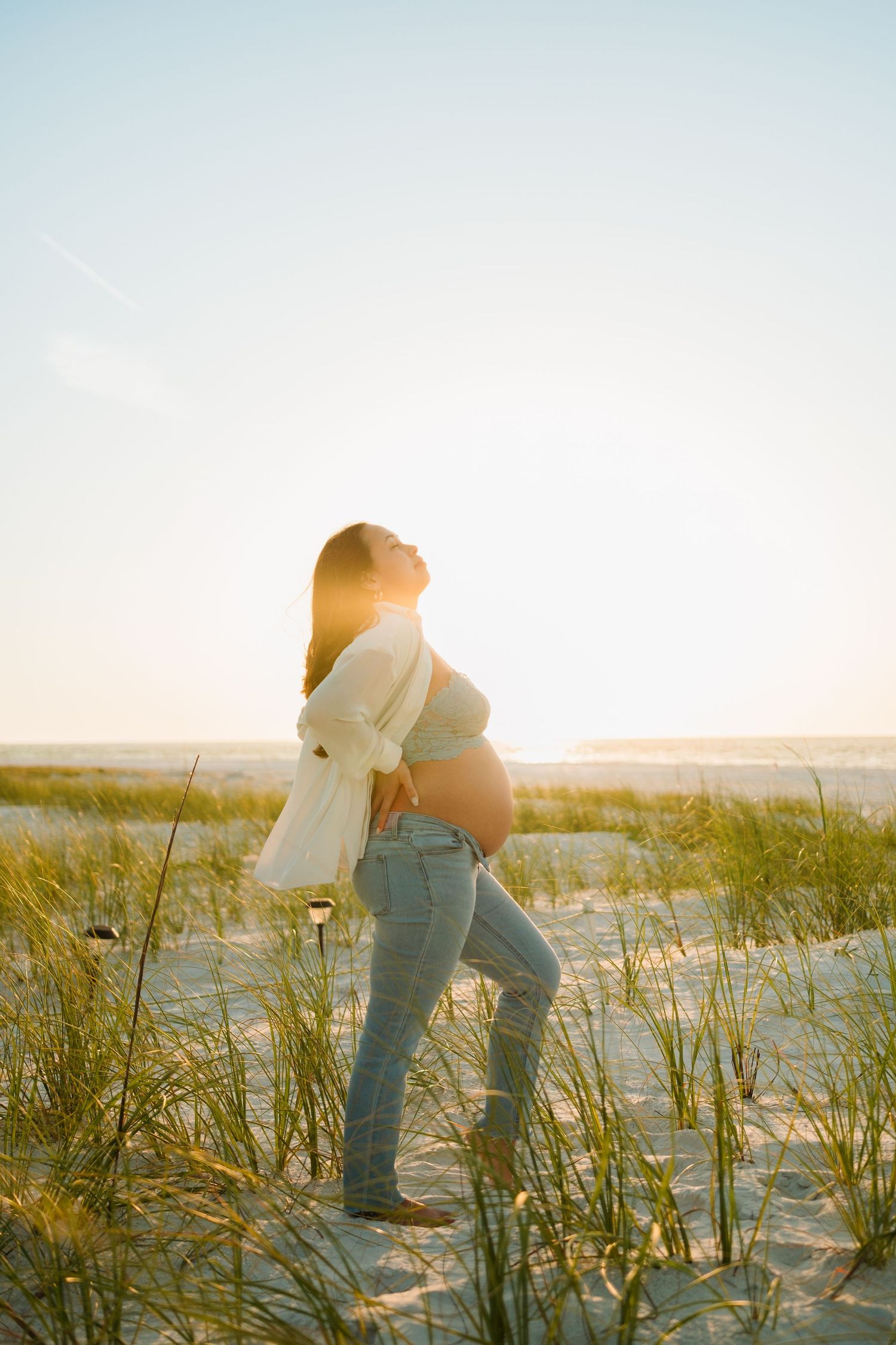 Two people walk through beach grass at sunset while holding hands, creating a romantic silhouette against the golden sky.