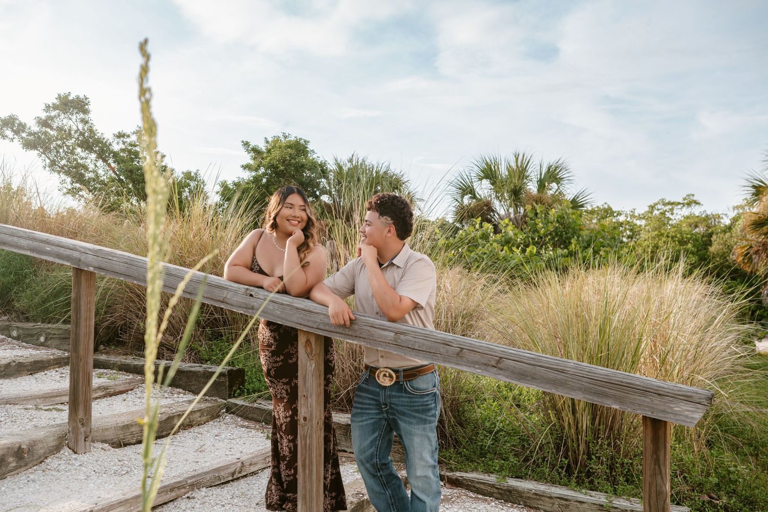 Couple laughing together on a wooden boardwalk surrounded by lush tropical greenery and palm trees on a sunny day.