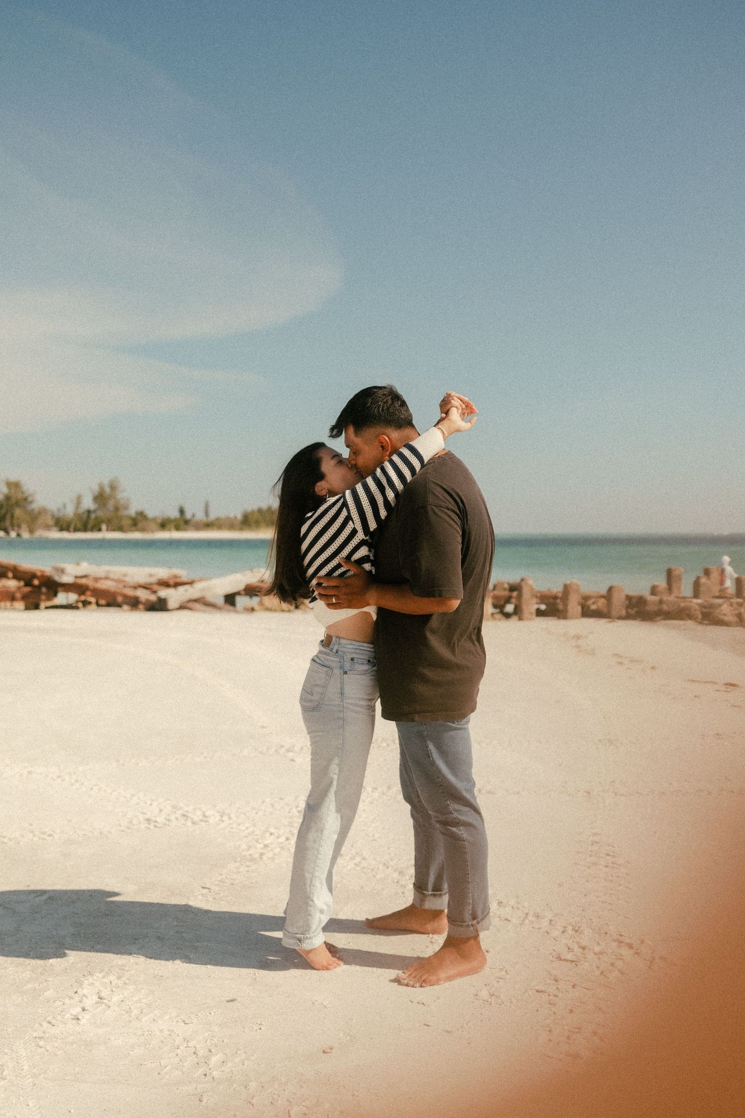 Couple embracing and dancing barefoot on a white sandy beach with turquoise water and blue sky.
