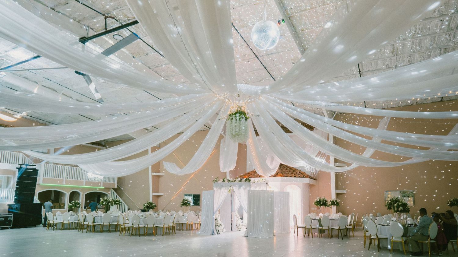 Grand wedding venue with white ceiling draping, fairy lights, and dance floor.