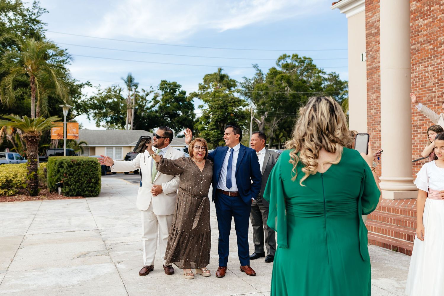 Wedding guests socializing outside brick church building on sunny day.