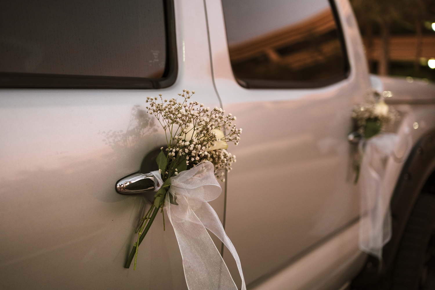 White wedding car door adorned with delicate baby's breath flowers tied with a white ribbon bow.