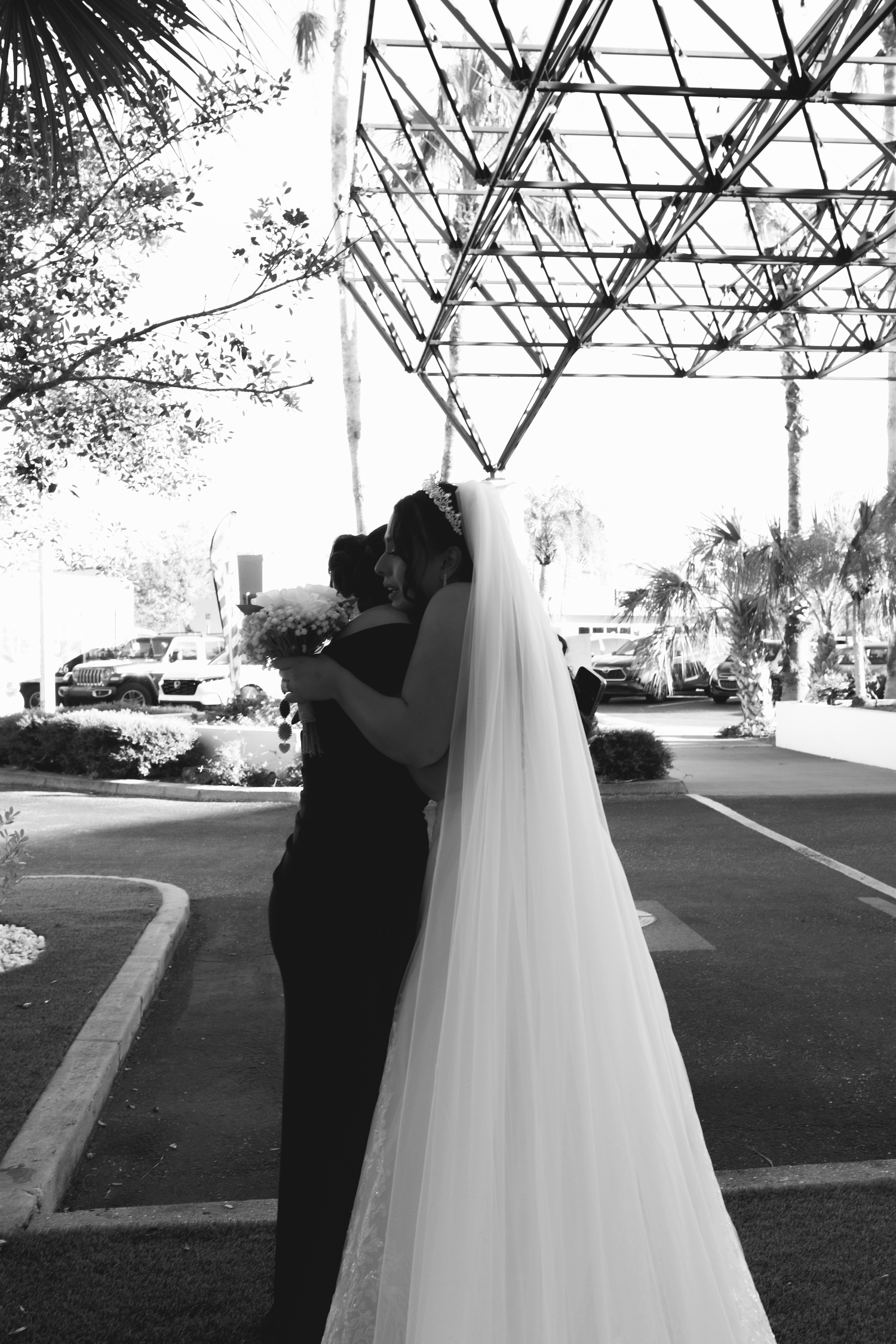 Black and white silhouette of bride and groom kissing under geometric canopy structure outdoors.