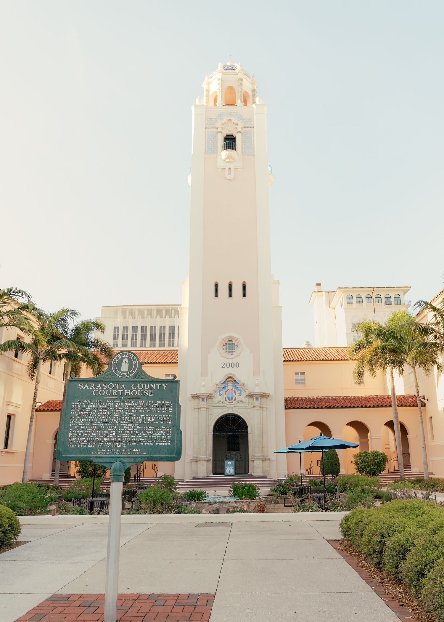 Sarasota County Courthouse with tall white tower, palm trees, and historic marker in Florida.