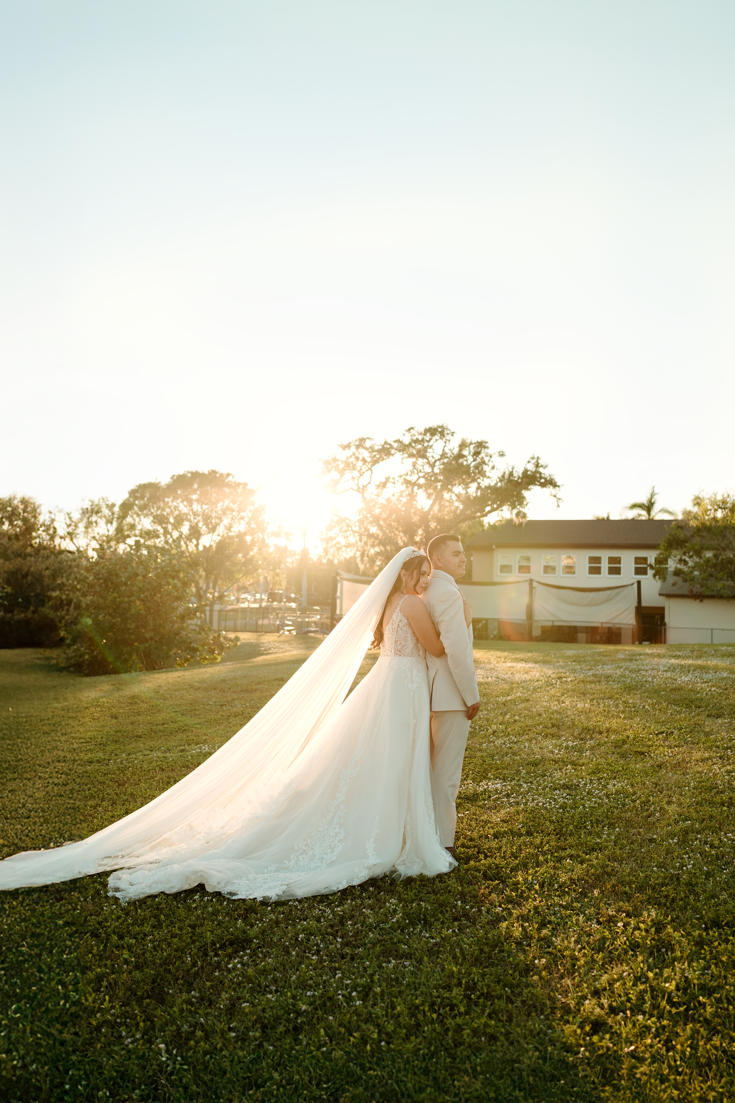 Bride and groom walk hand in hand across a green lawn during a golden sunset at their wedding.