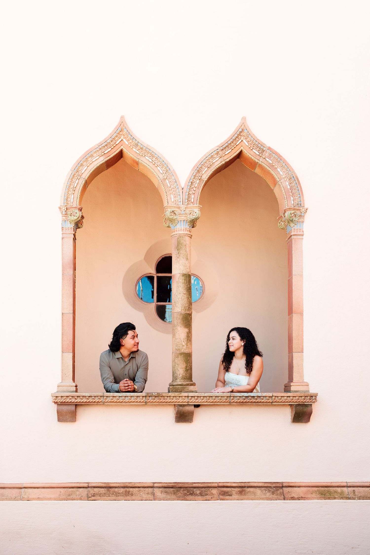 Couple sitting in ornate Moorish-style double arch alcove with decorative column and circular window.