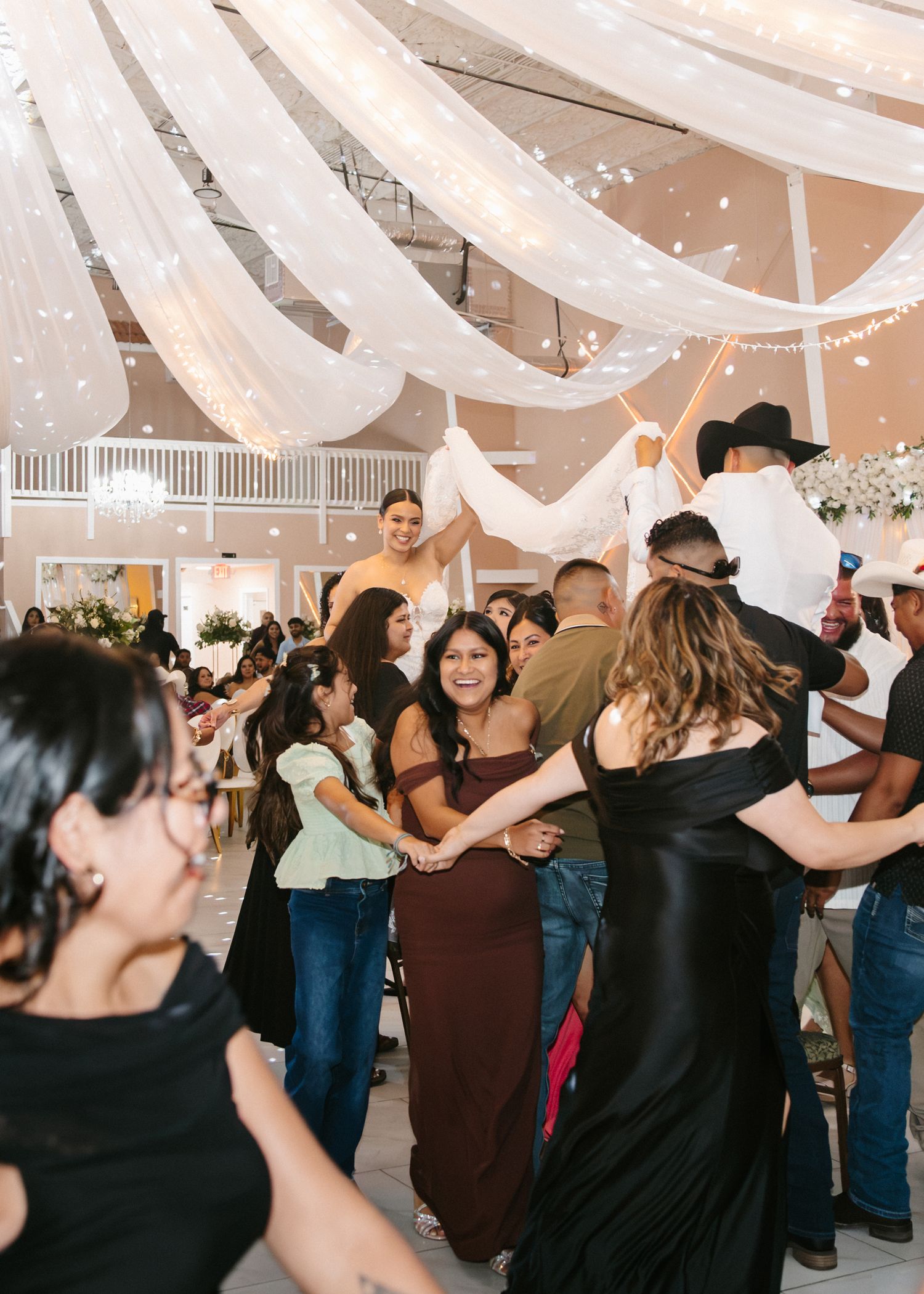 Wedding guests dancing and celebrating on decorated reception dance floor.