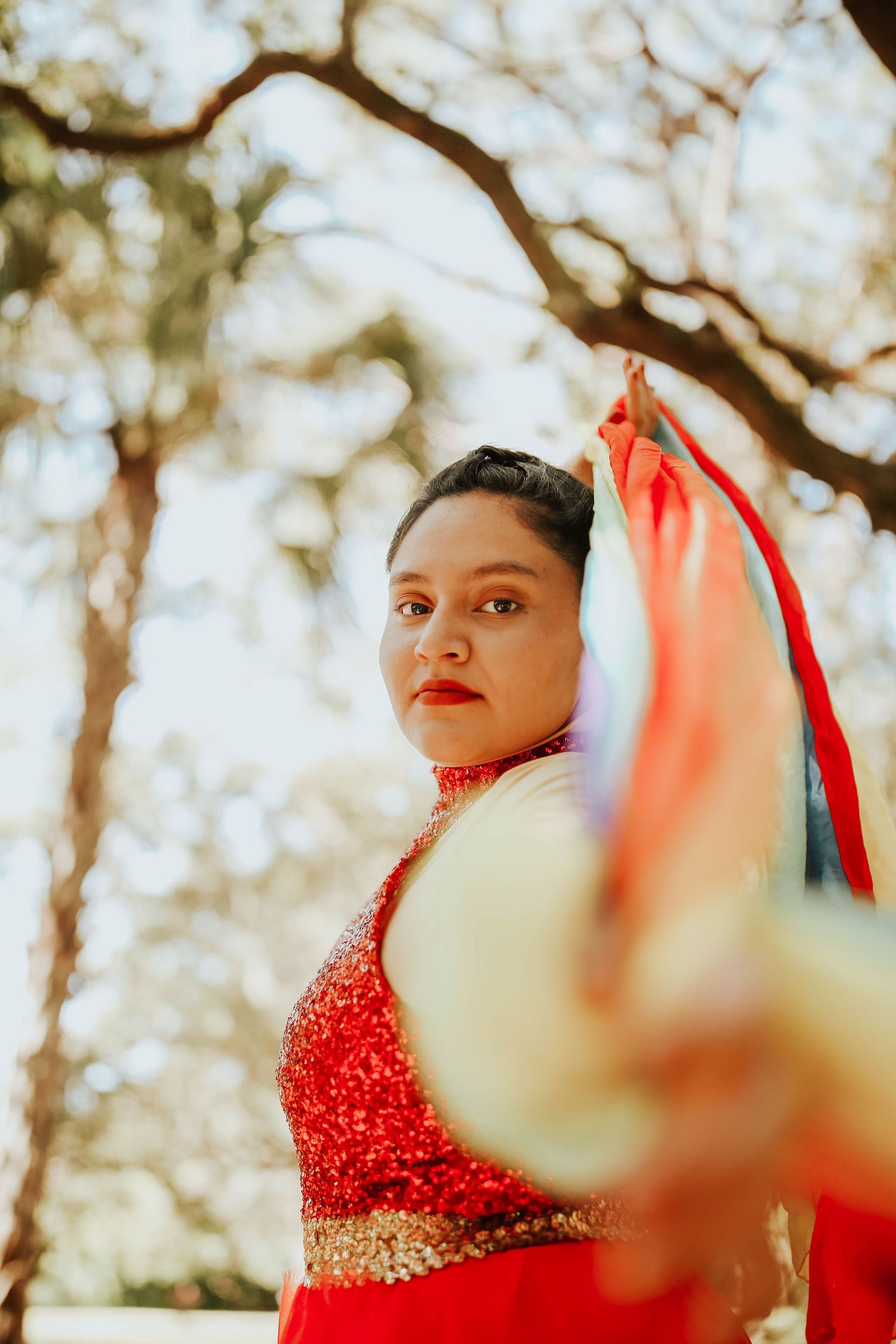 Artistic portrait in red sequined dress with dramatic sunlit background.