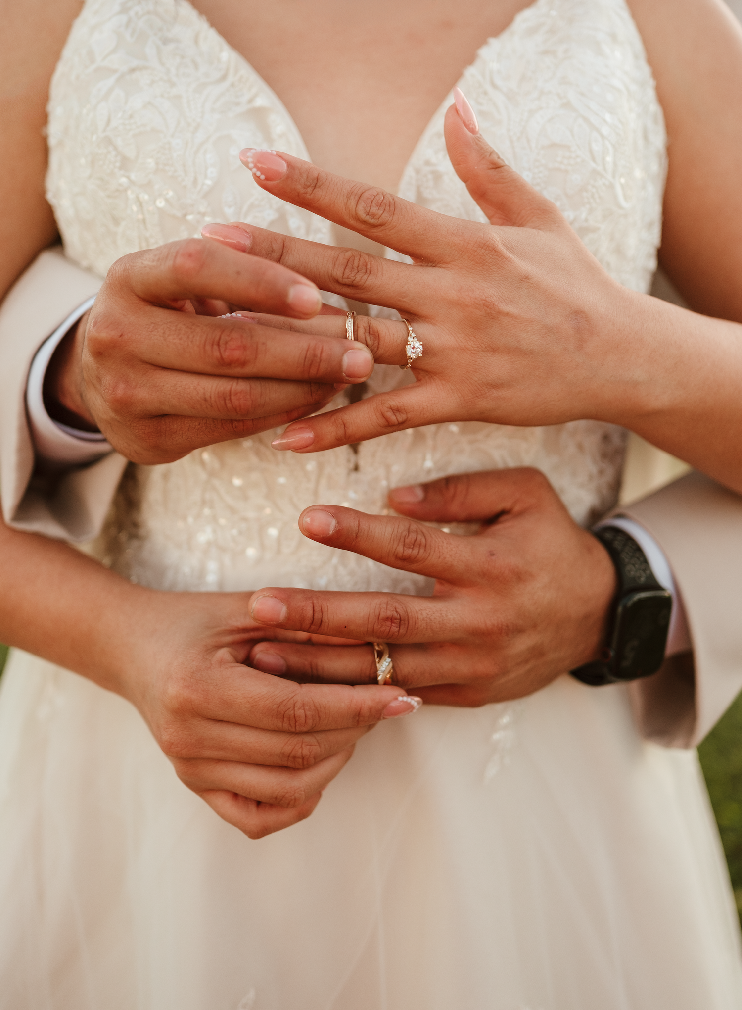 Close-up of bride and groom displaying wedding rings and engagement ring in elegant lace wedding attire.