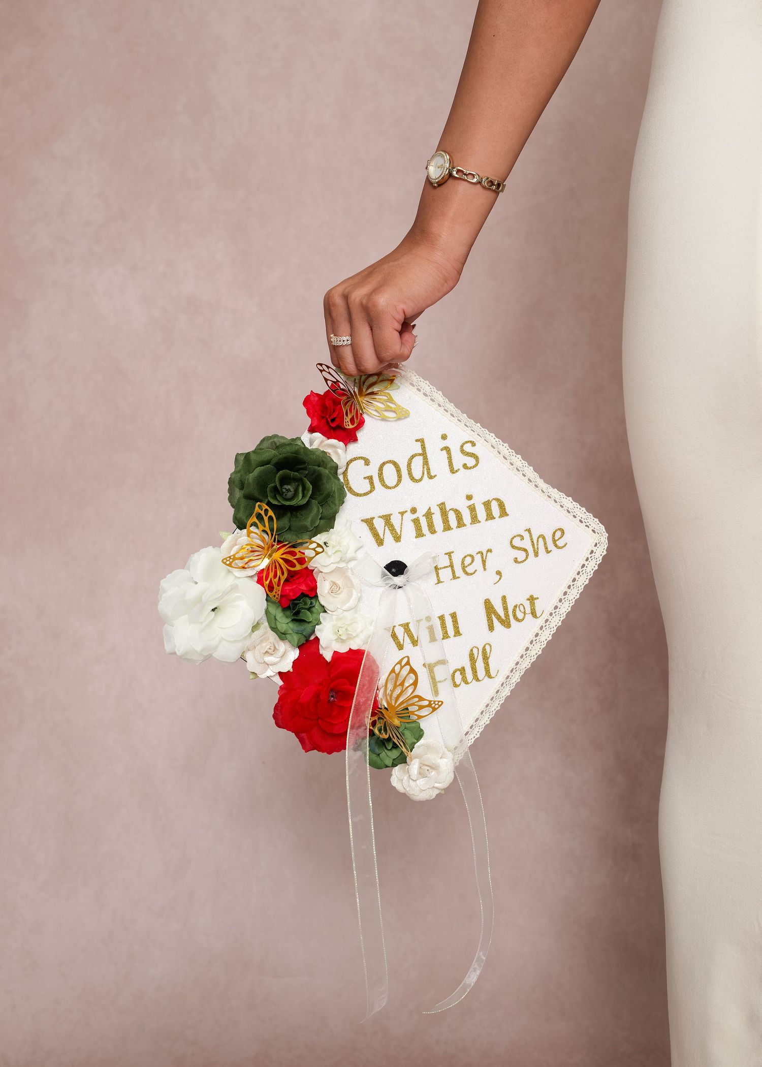 Decorated graduation cap with floral arrangement and gold text reading God is Within Her, She Will Not Fall.