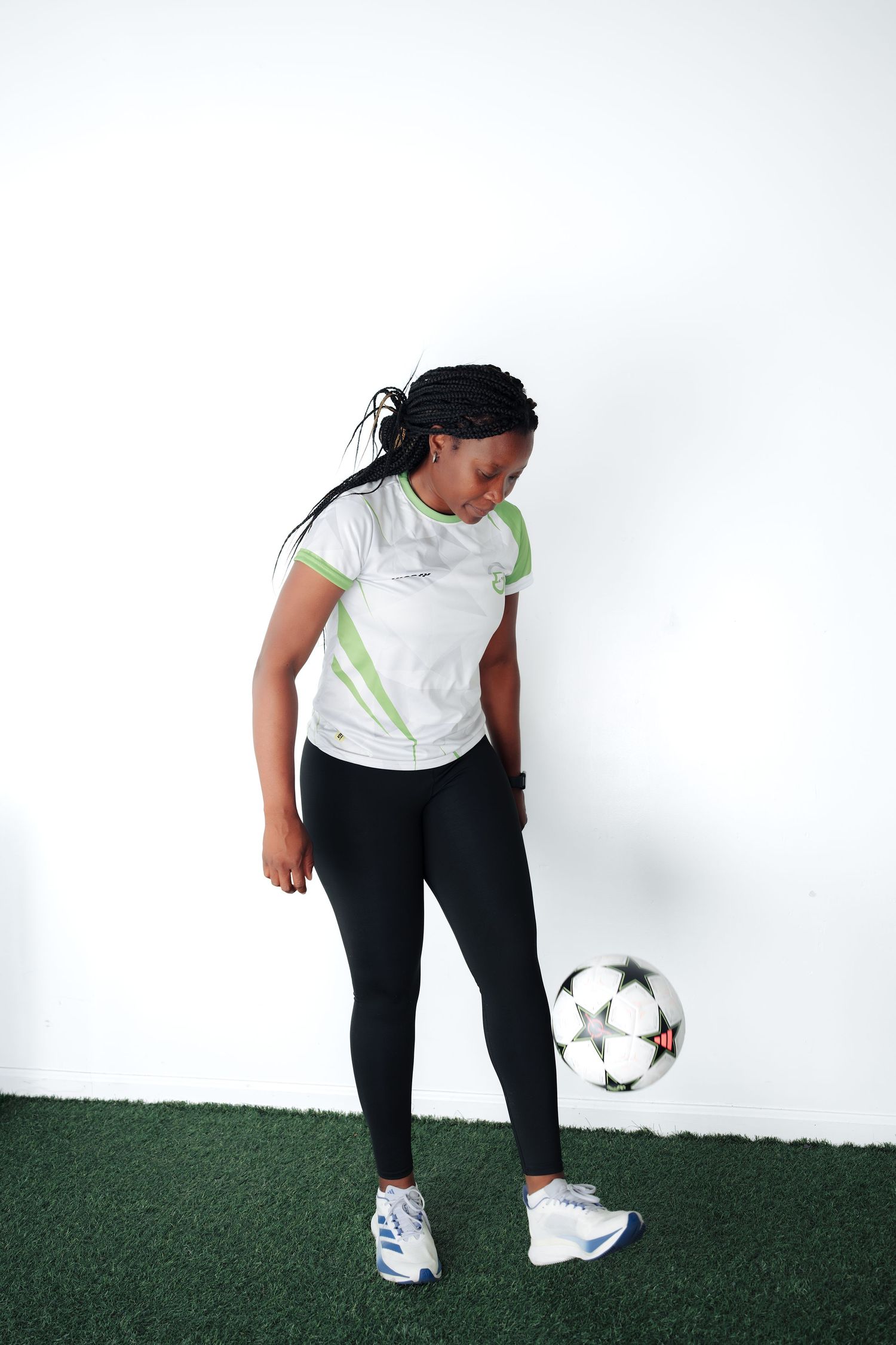 Young Black female soccer player juggling a football in sportswear on artificial grass against white background.