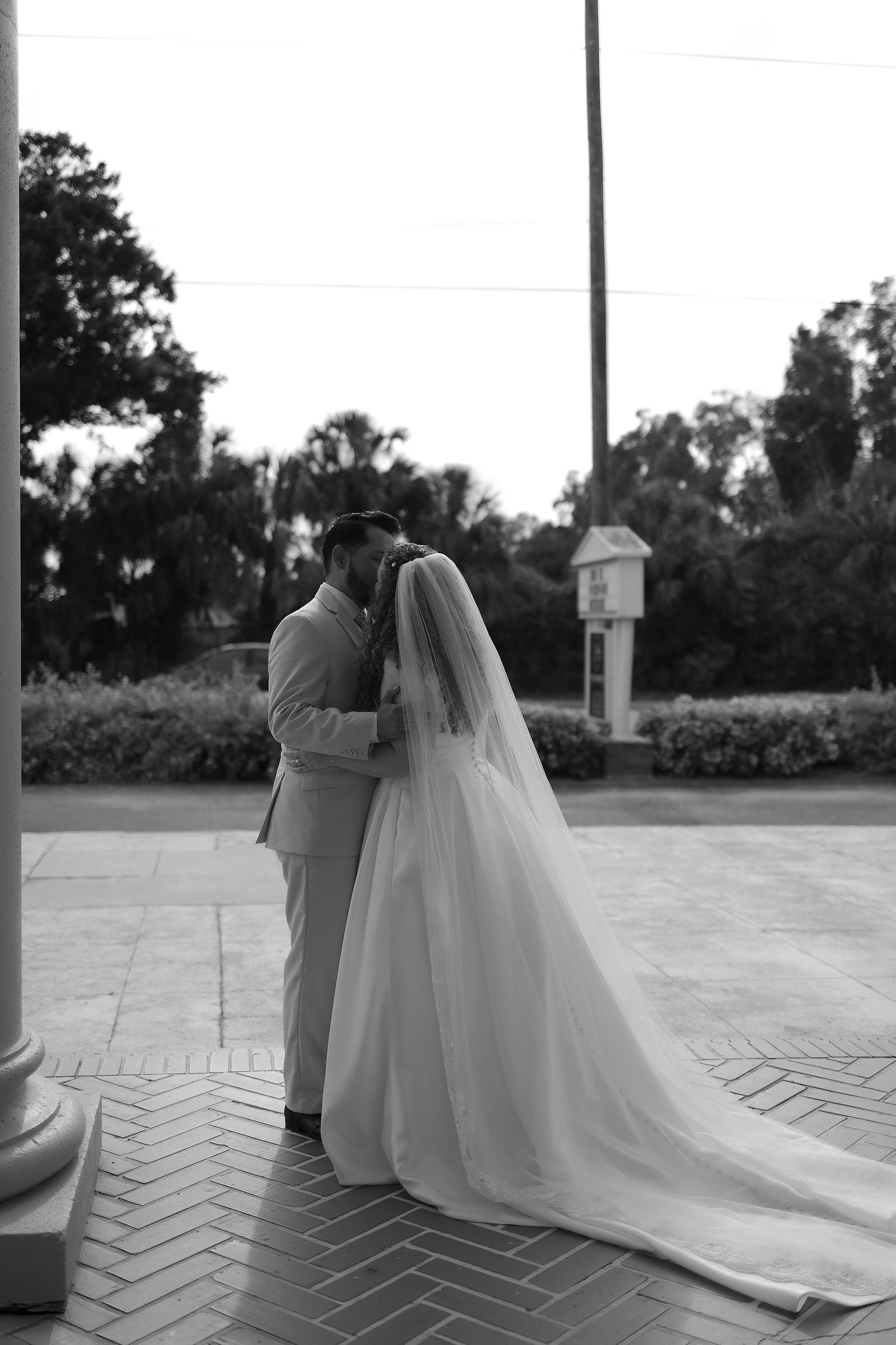Black and white photo of bride and groom sharing first kiss outdoors after wedding ceremony.