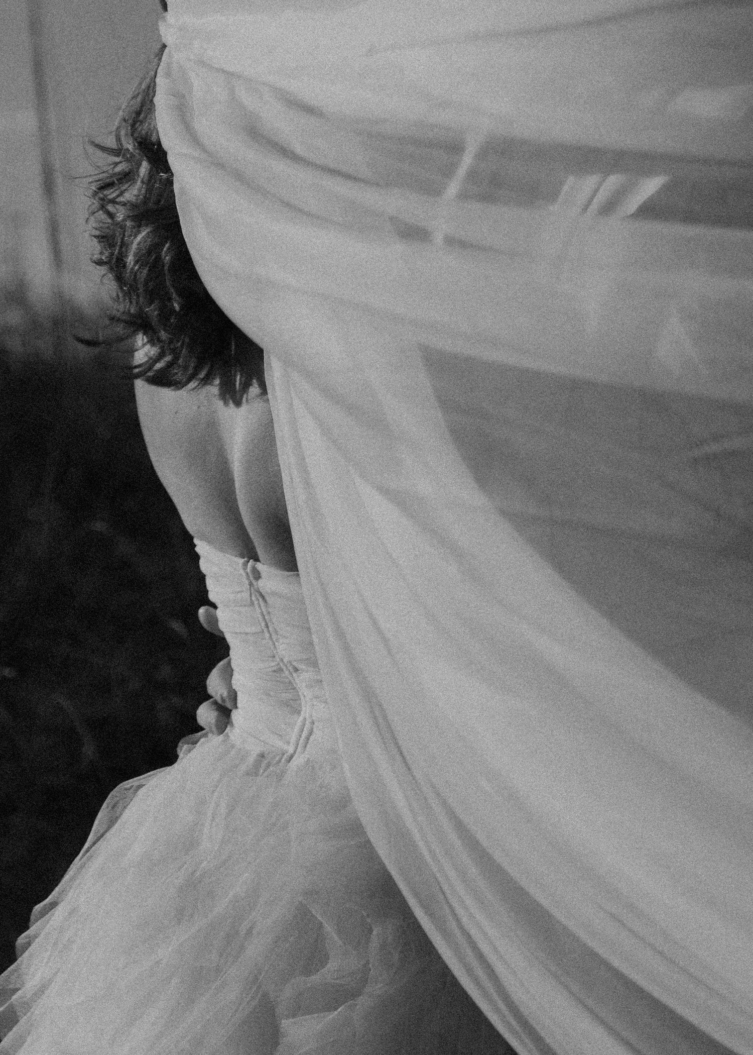 Black and white photo of a bride in a flowing wedding gown with veil billowing around her.