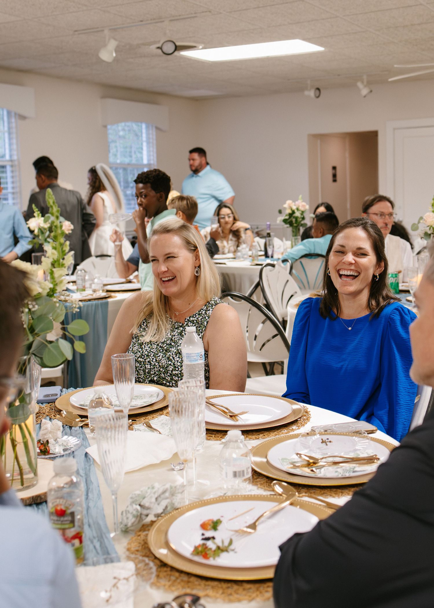 Laughing women guests enjoying wedding reception dinner at elegantly set table.