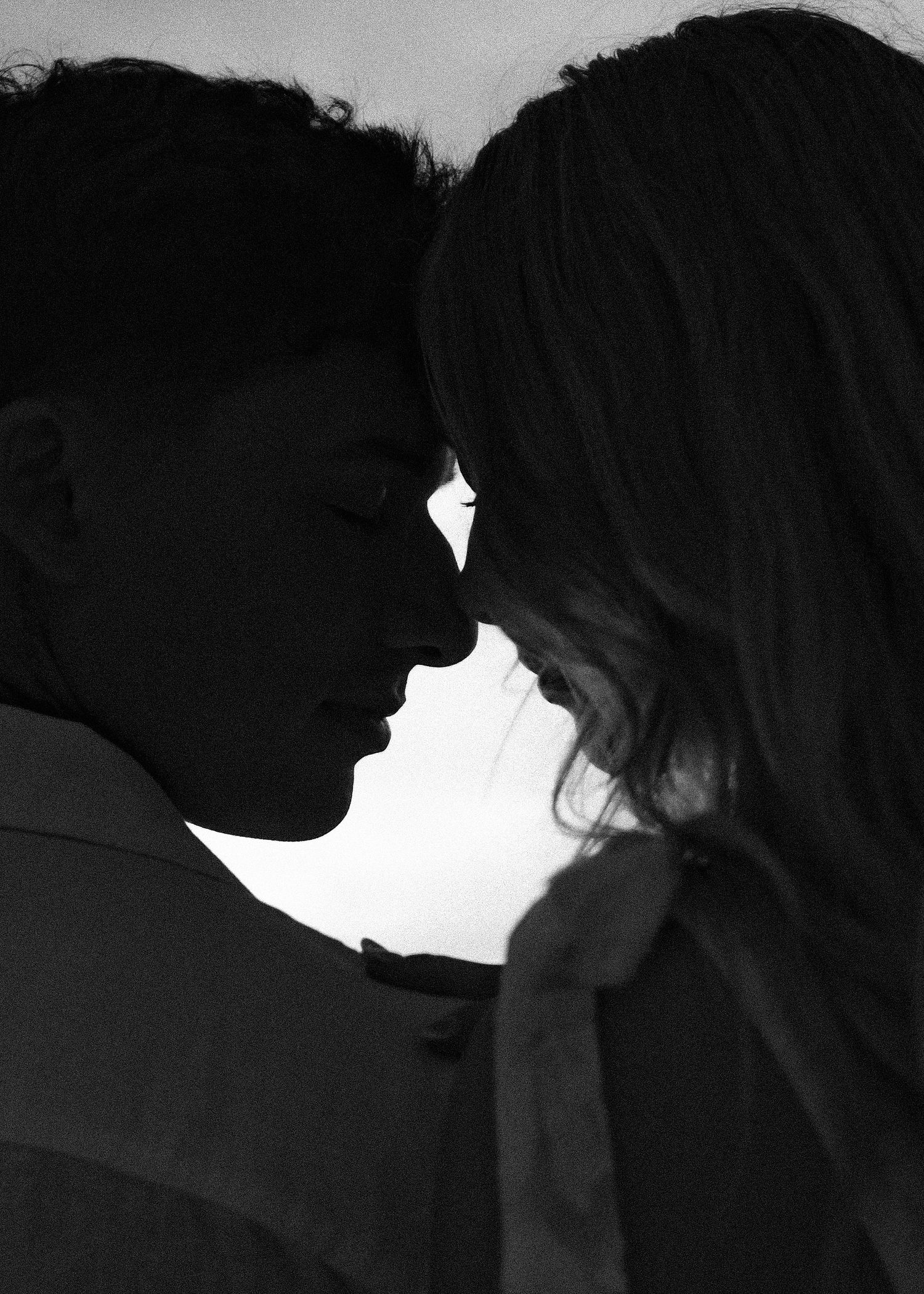 Black and white silhouette of a romantic couple with foreheads touching, sharing an intimate moment.
