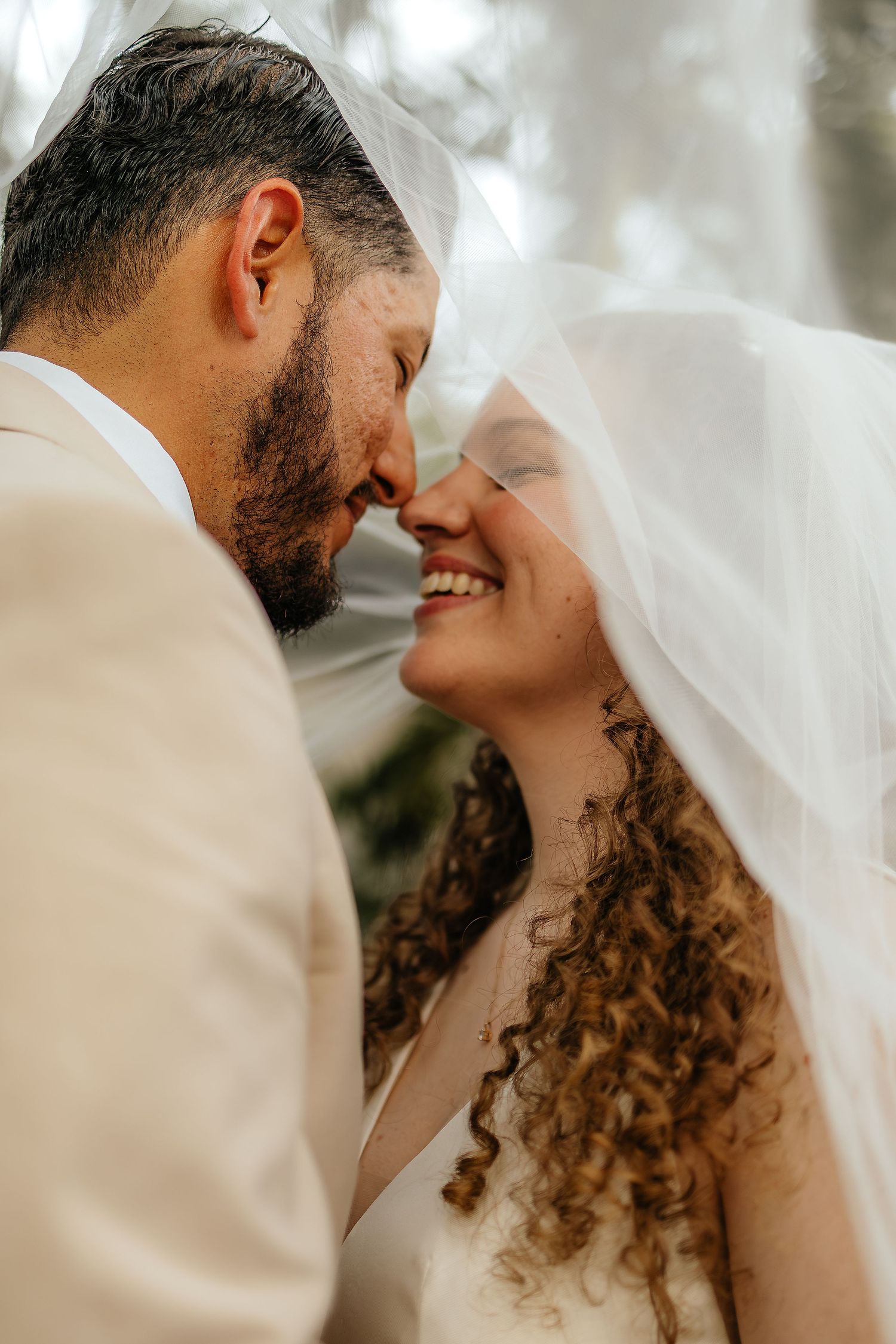 Romantic close-up of bride and groom sharing an intimate moment under a sheer veil on their wedding day.