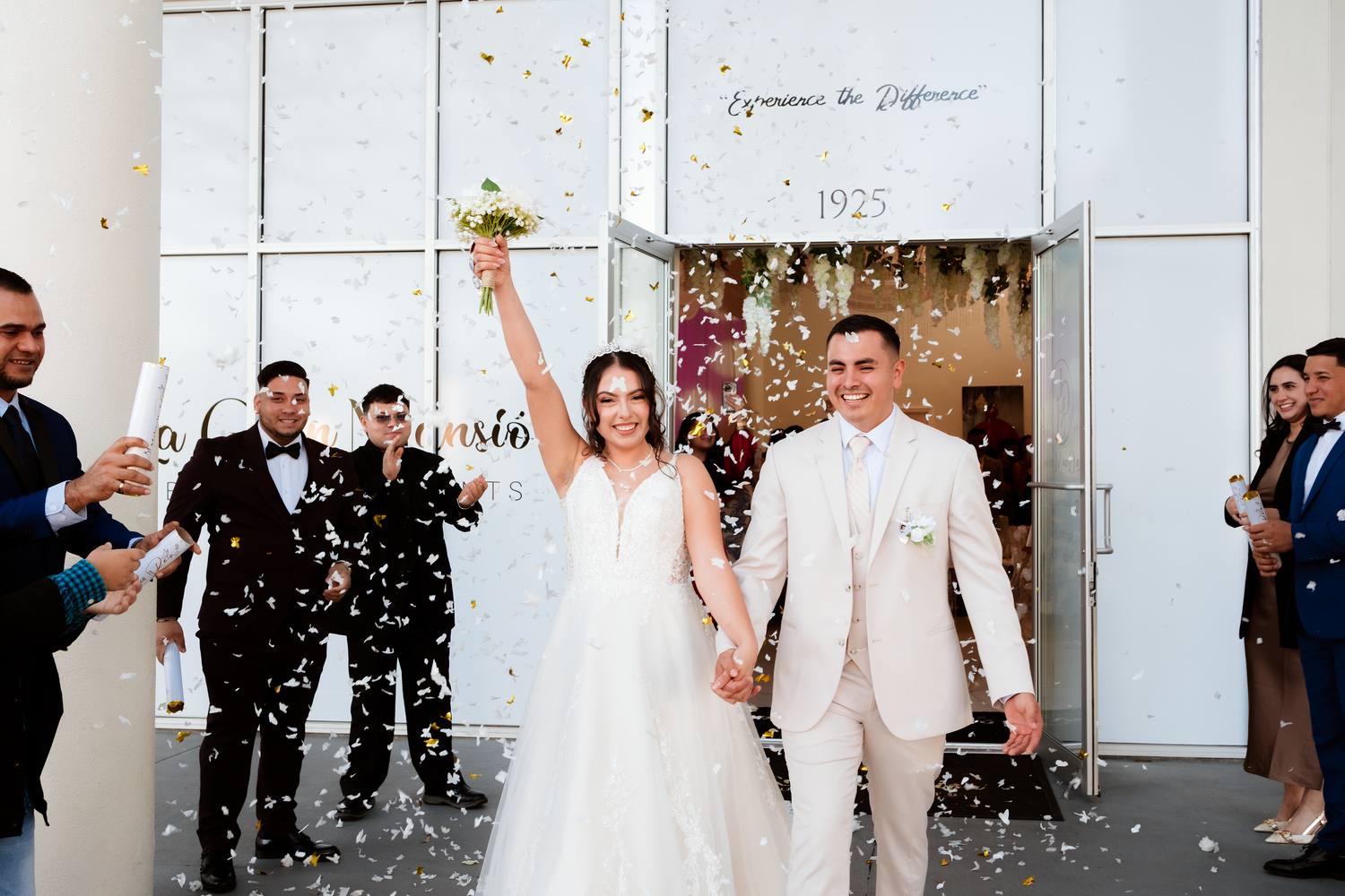 Joyful newlyweds exit wedding venue hand-in-hand as colorful confetti fills the air around them.