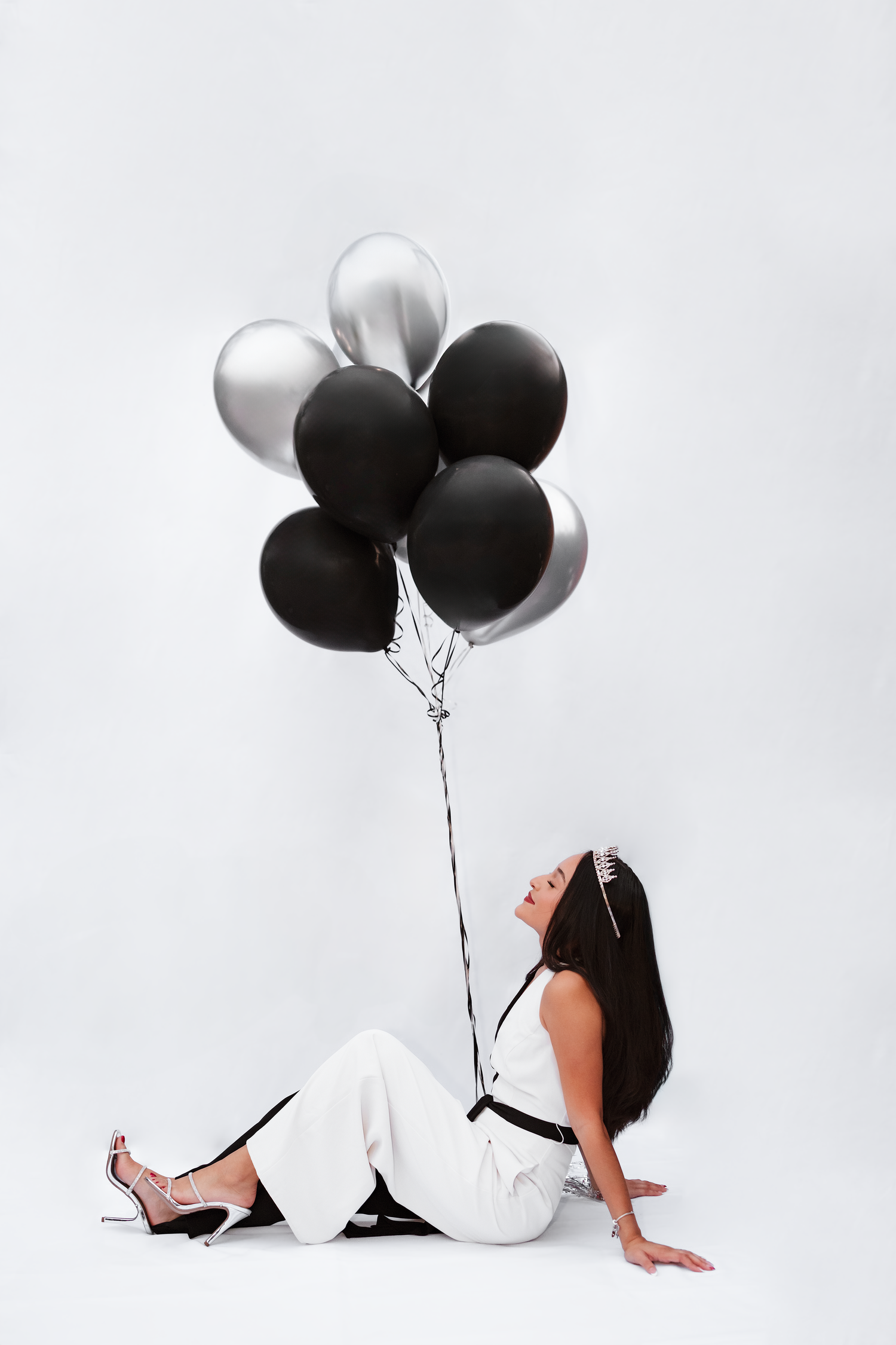 Black and white portrait of someone in white clothing holding black and silver balloons against a light background.