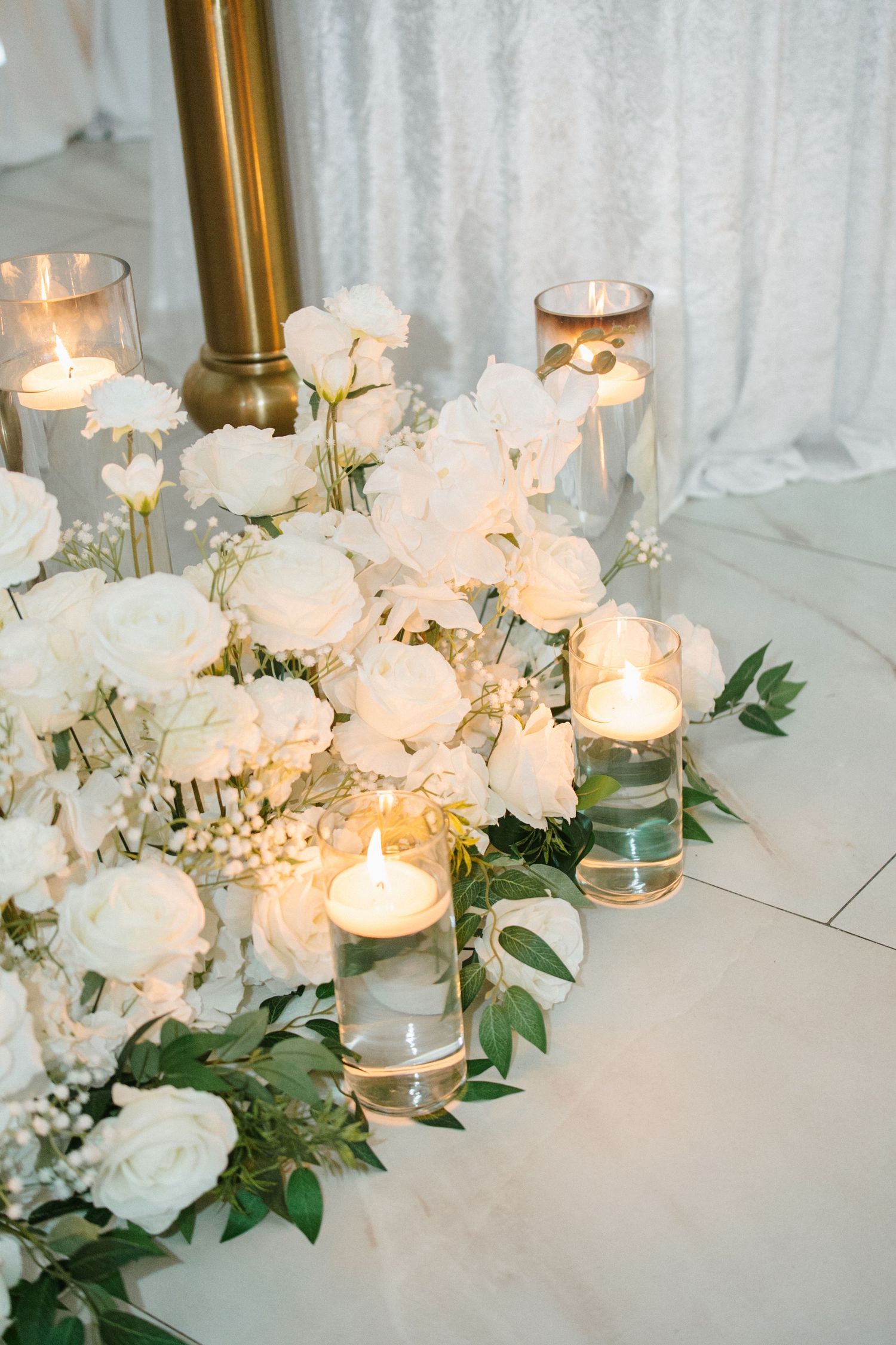 White roses and candles in glass holders decorate wedding altar floor.