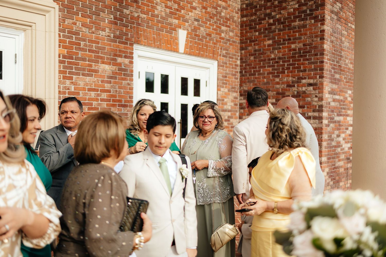 Wedding guests mingle outside a brick building following a ceremony reception gathering.