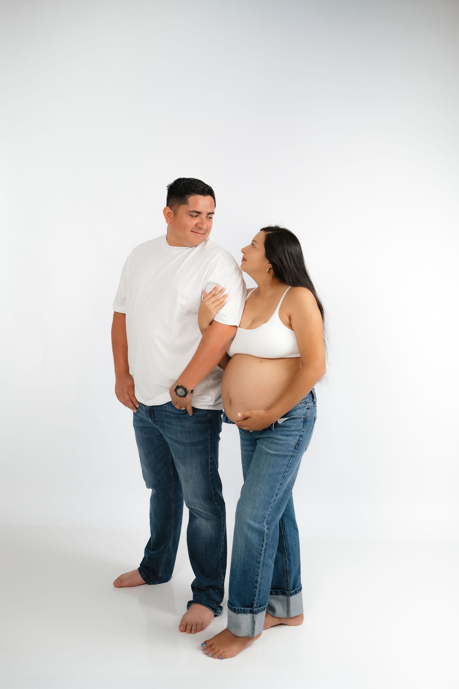 Expecting couple in white tops and jeans sharing a tender moment during maternity photo session.