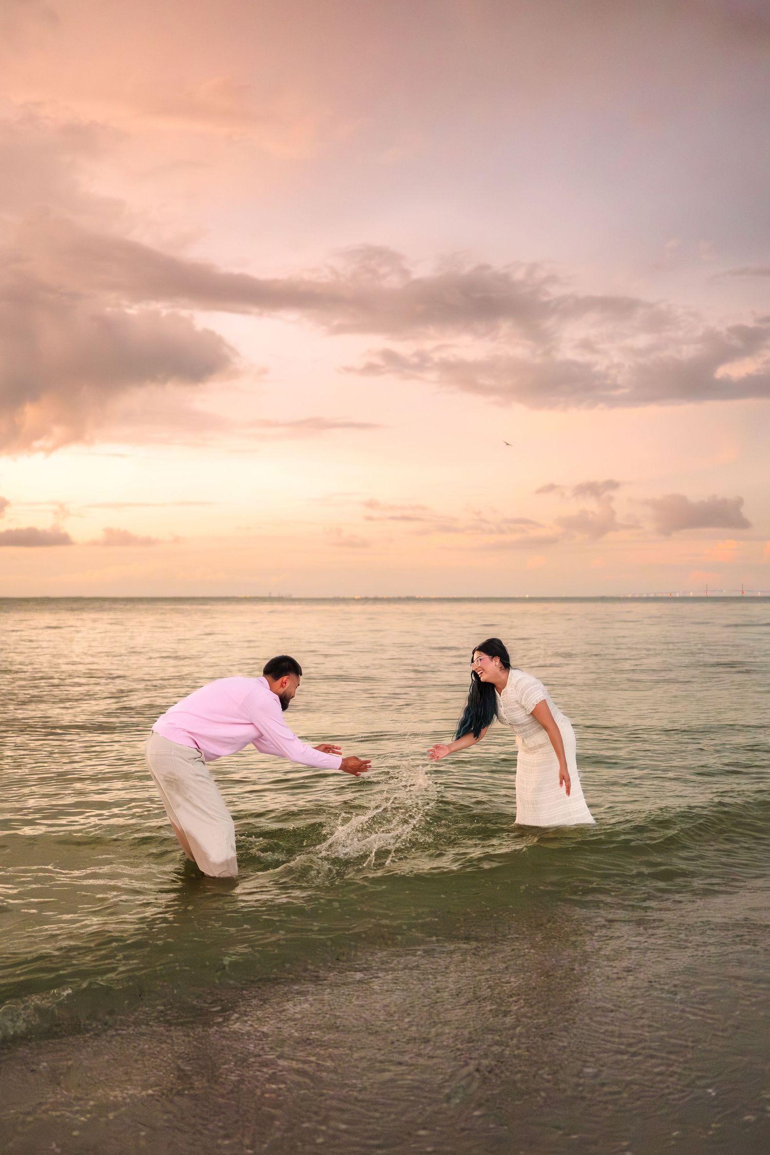 A couple in white clothing releases a lantern into the ocean at sunset creating a romantic beach scene.