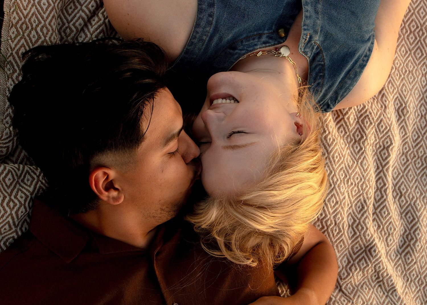 Couple lying down sharing a romantic kiss, with golden hour sunlight illuminating their faces.