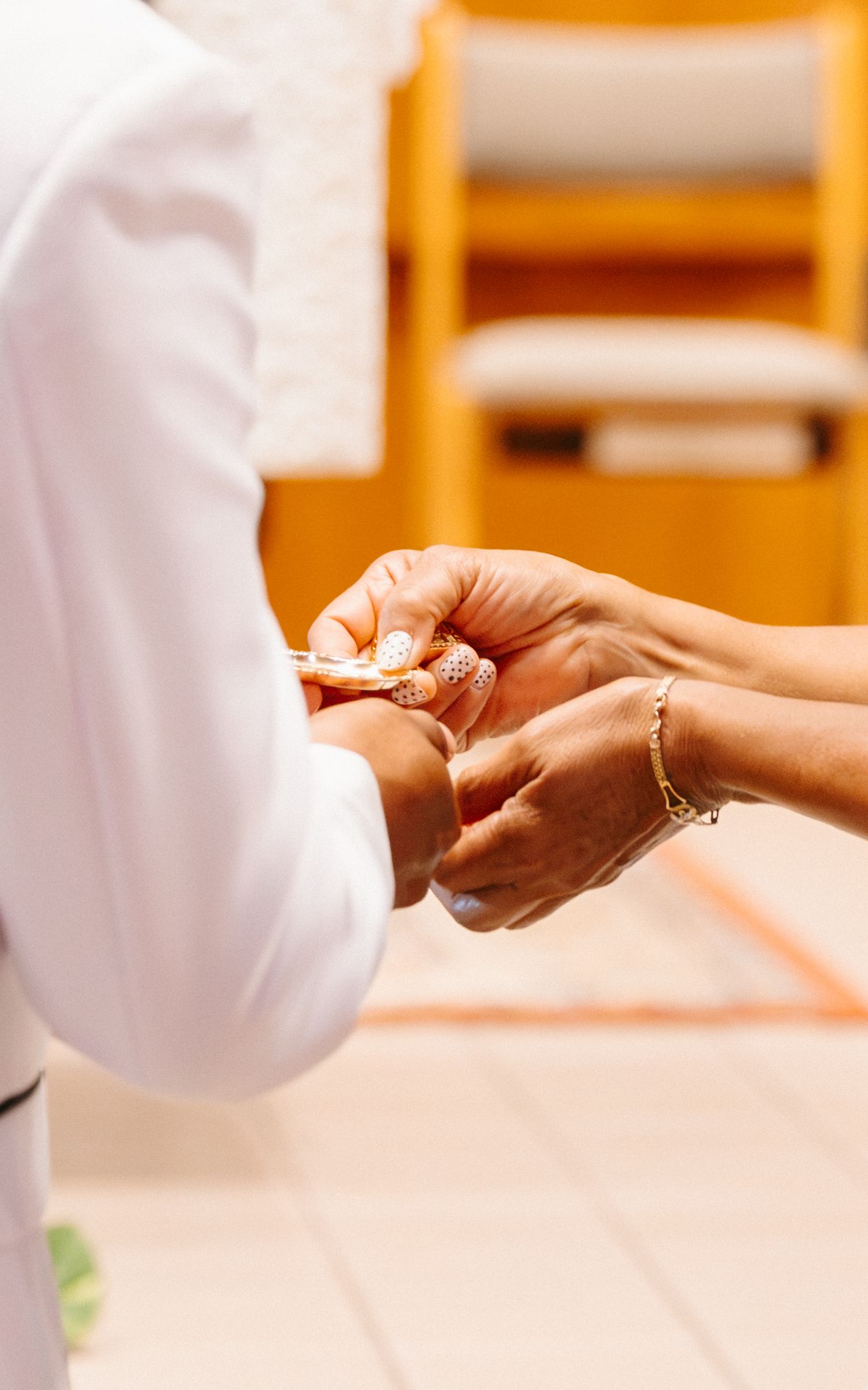 Close-up of hands exchanging wedding rings during a ceremony, with one person wearing a white suit.