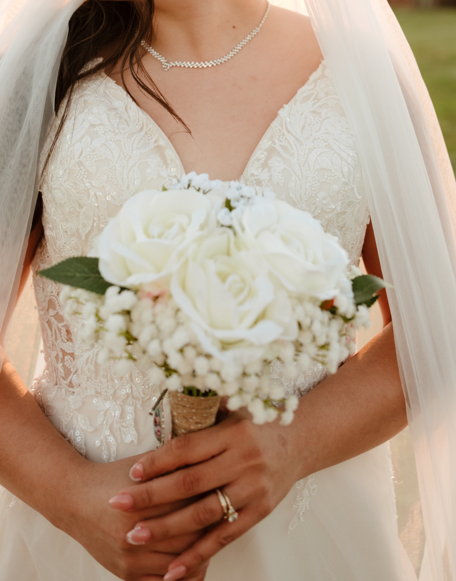 Close-up of bride holding elegant white rose bouquet with baby's breath, wearing lace gown and veil.