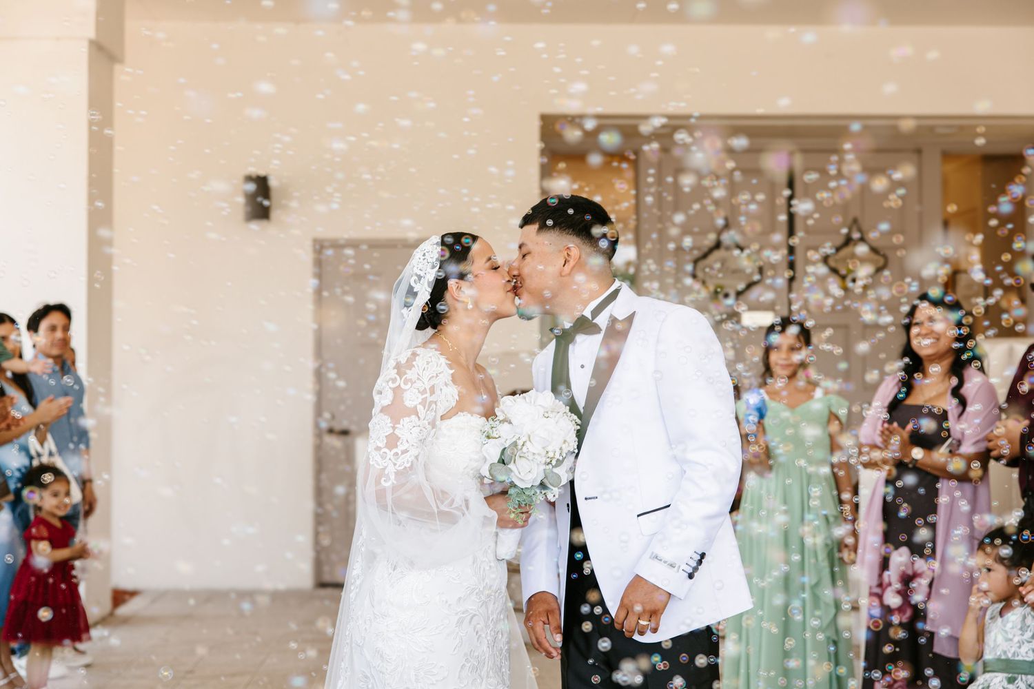 Newlywed couple sharing a kiss surrounded by bubbles during their wedding ceremony exit.