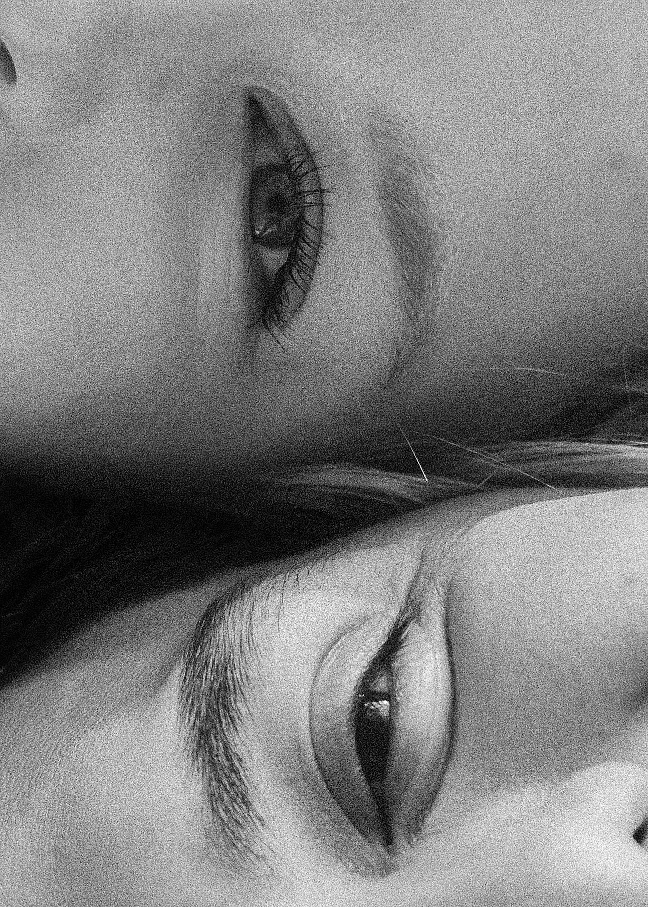 Black and white close-up photo of two people's eyes and eyebrows facing opposite directions.