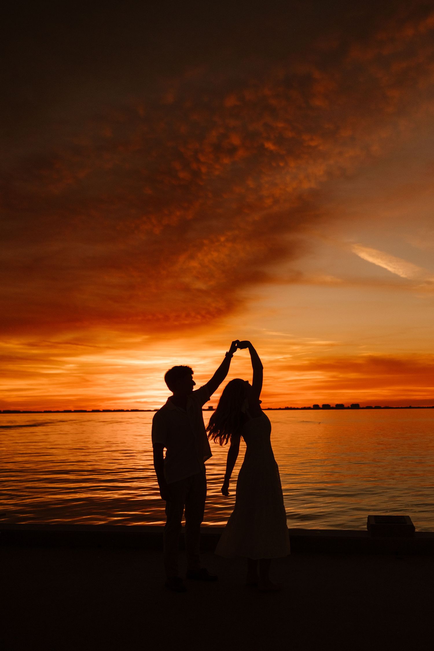 Silhouette of a couple dancing romantically by the water during a stunning red and orange sunset.
