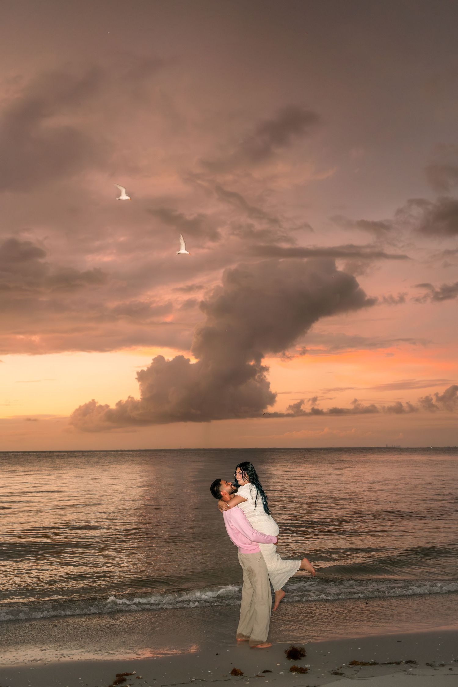 A romantic sunset beach photoshoot silhouetted against an orange and pink sky over the ocean.
