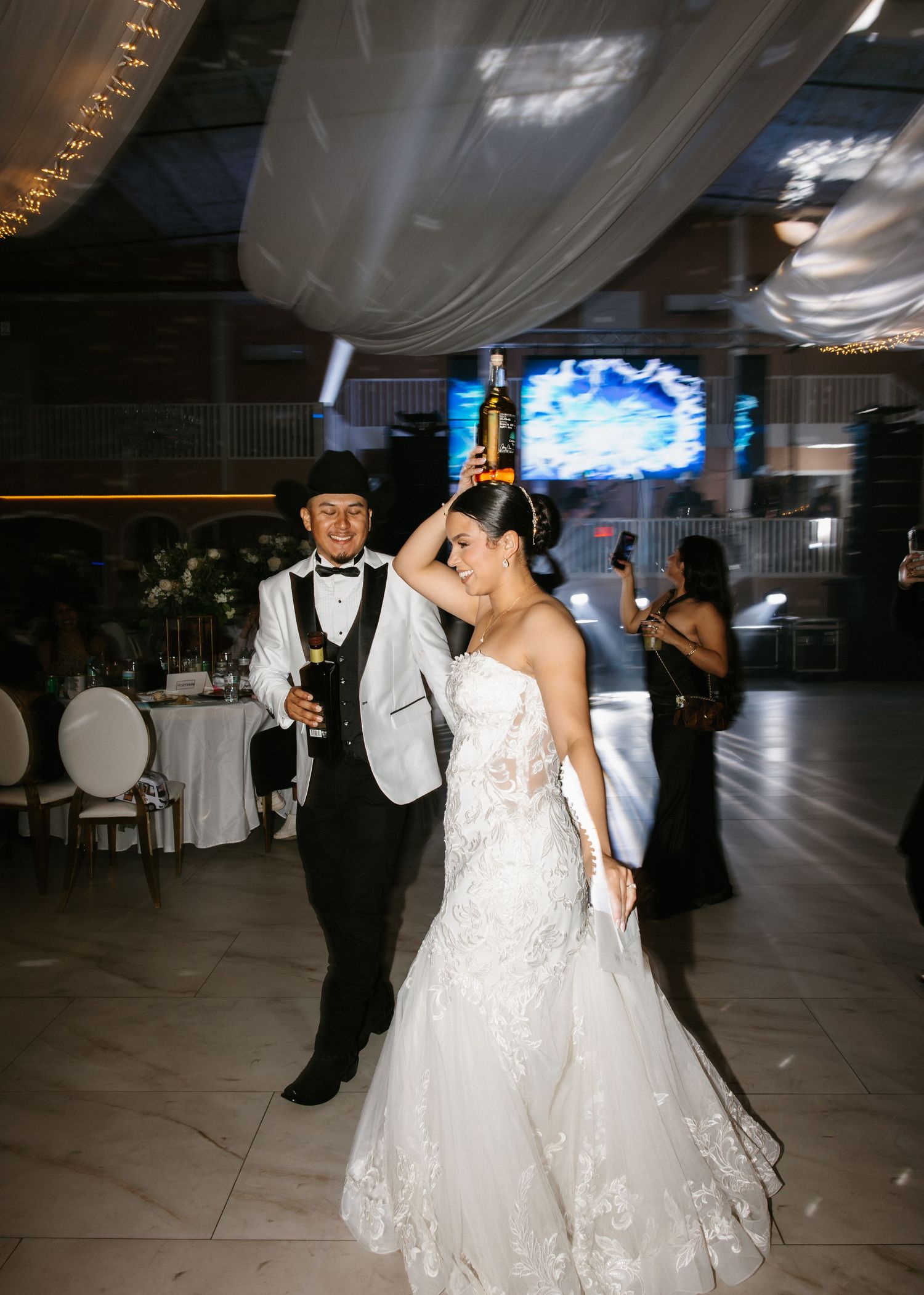 Bride in lace mermaid gown dances with groom in white tuxedo jacket on wedding reception dance floor.