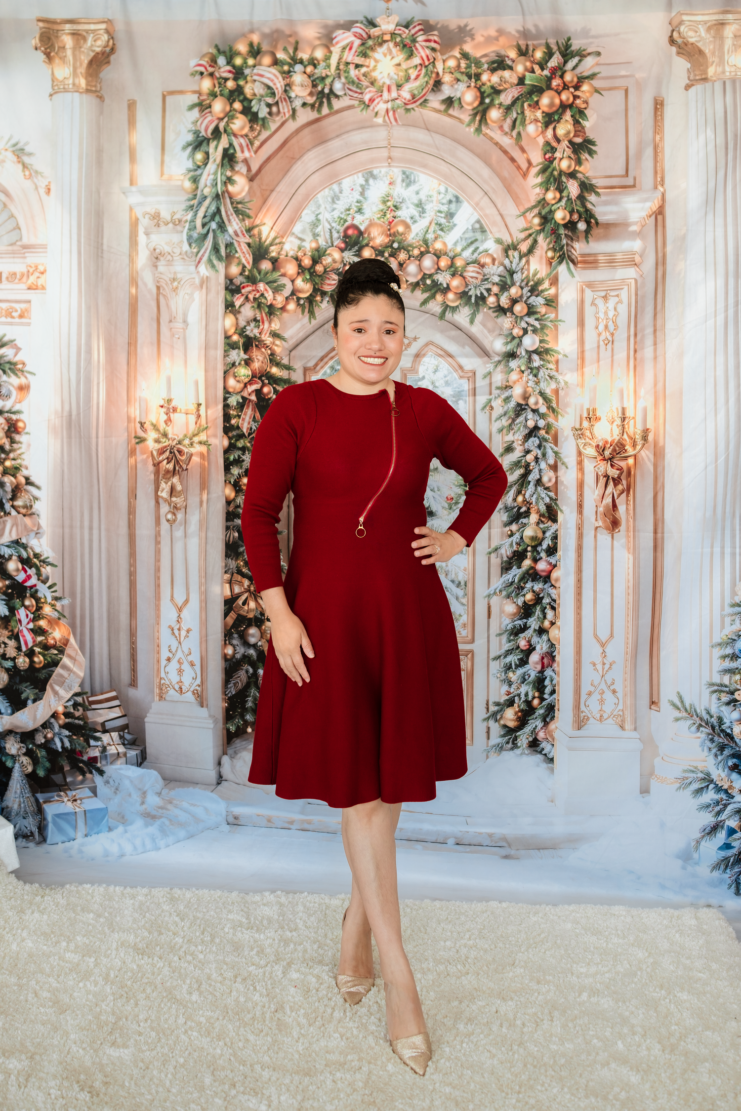 A festive red dress with gold heels stands against an elegant archway decorated with floral garlands and winter decor.