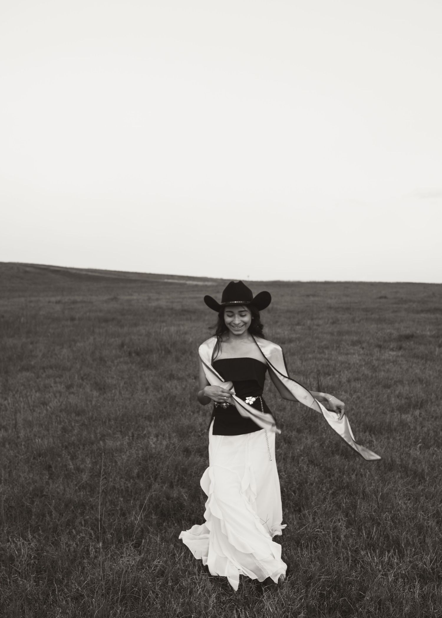 Woman in cowboy hat and white skirt dancing in open field, black and white photography.