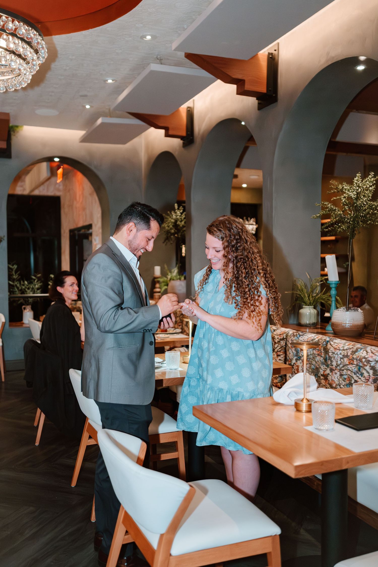 Couple sharing a romantic moment in an elegant restaurant with arched walls, wooden tables, and soft lighting.