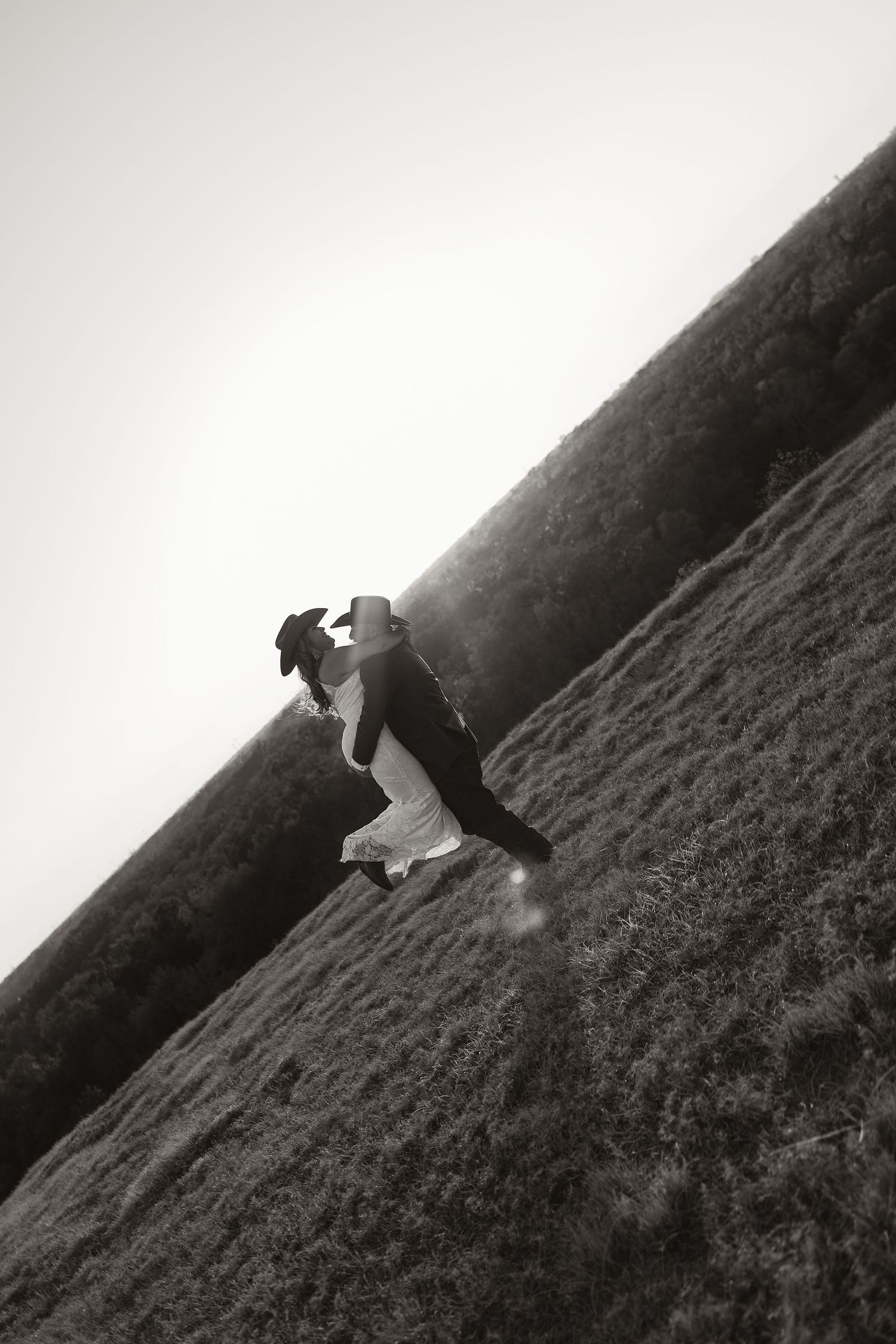 Bride and groom sharing romantic kiss on a hillside meadow in artistic black and white wedding portrait.
