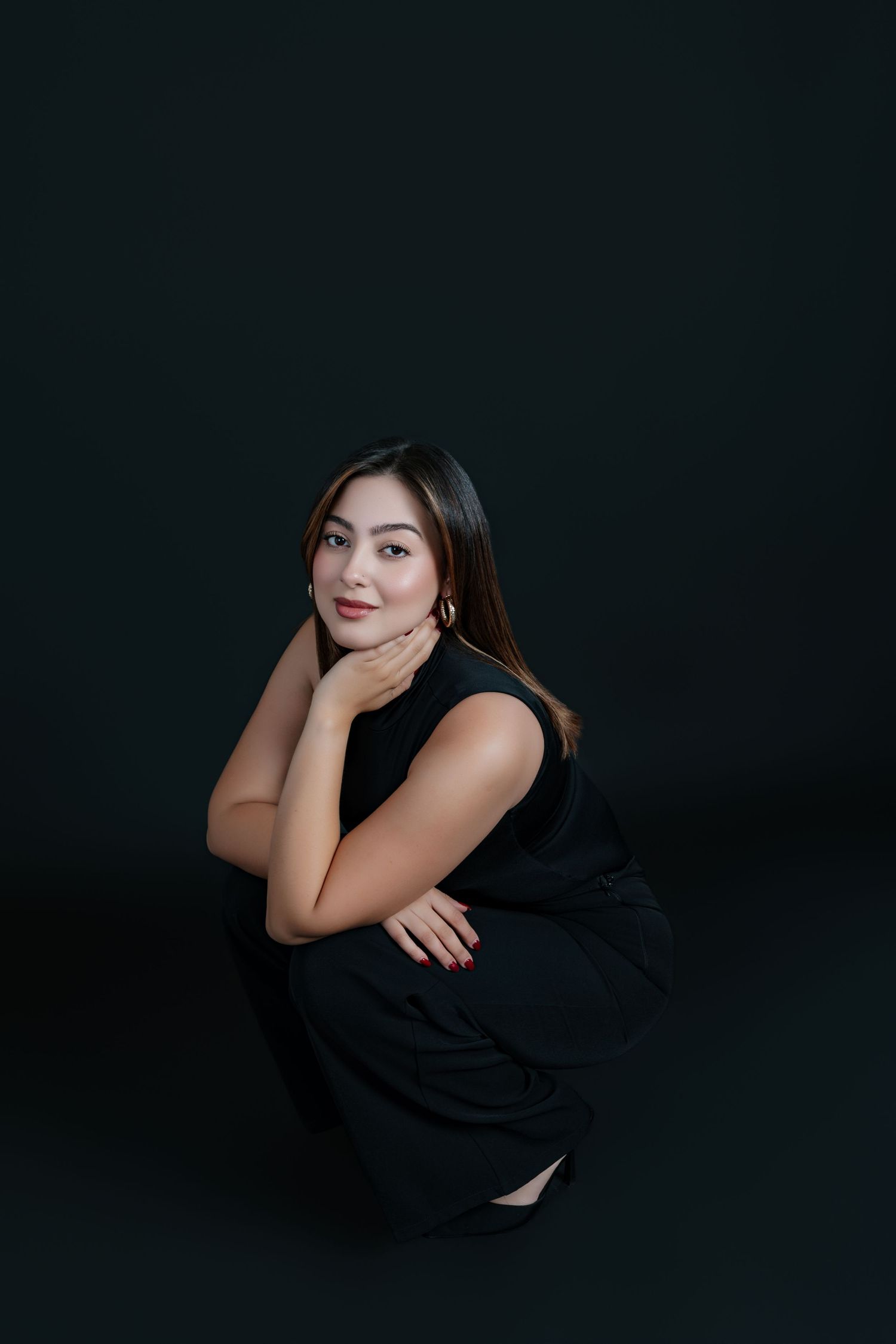 A young Asian woman in a black dress poses gracefully against a dark background, resting her chin on her hand.