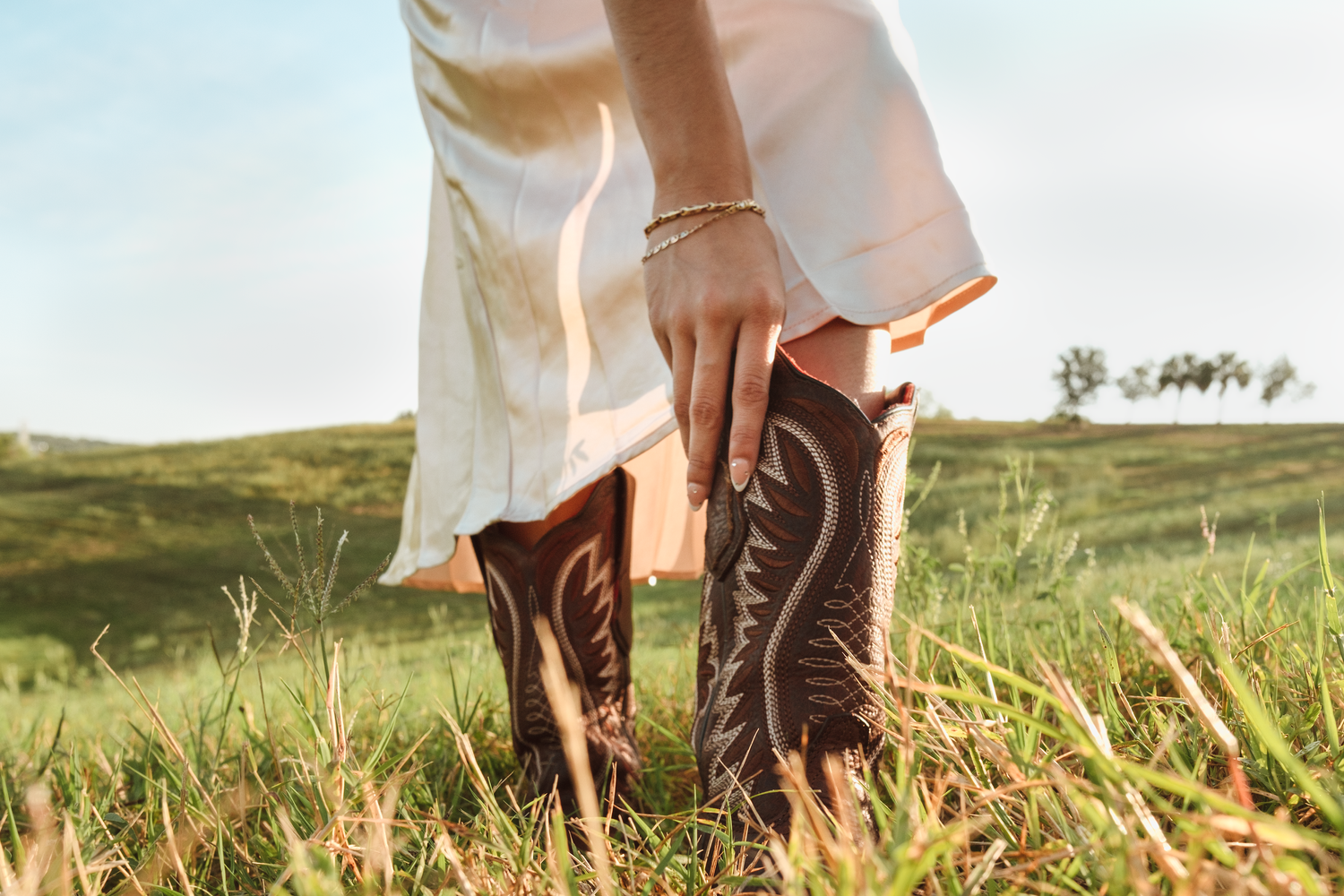 Brown leather cowboy boots worn in a grassy meadow at golden hour.