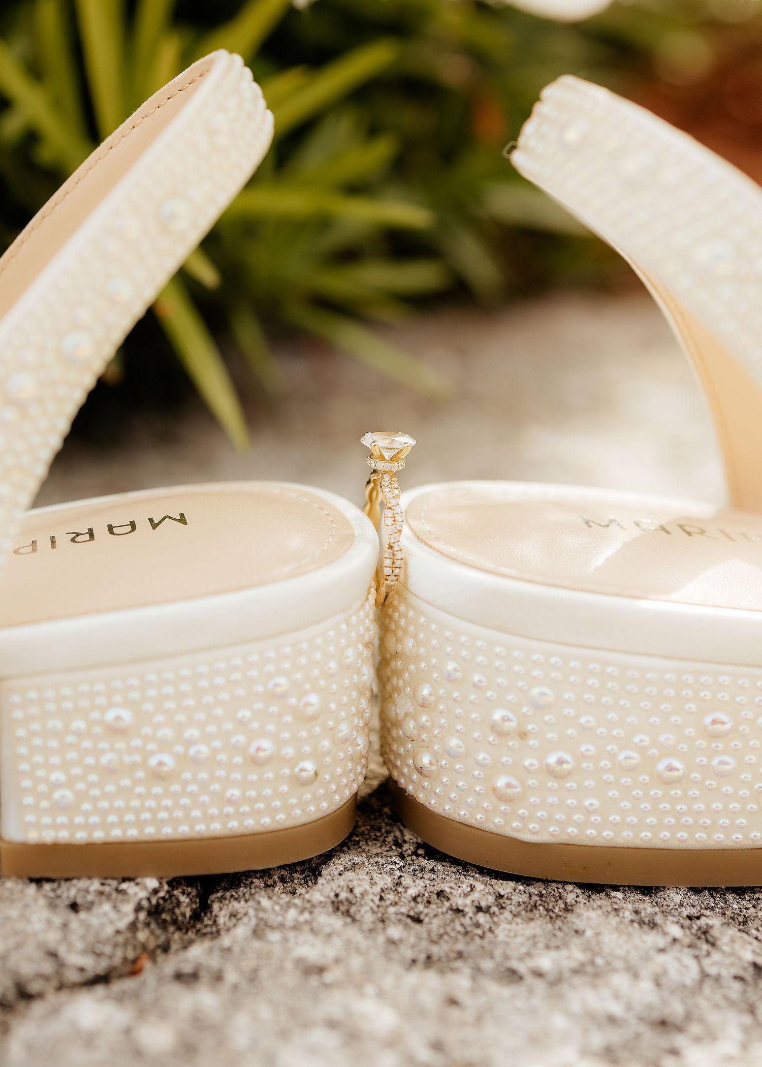 Pearl-embellished bridal wedge sandals by Marip displayed on stone surface with a delicate ring charm accent.