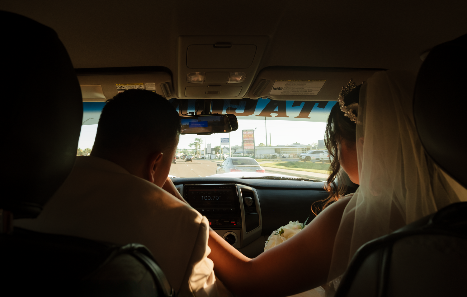 Newlywed couple in wedding attire driving away in a car after their wedding ceremony.