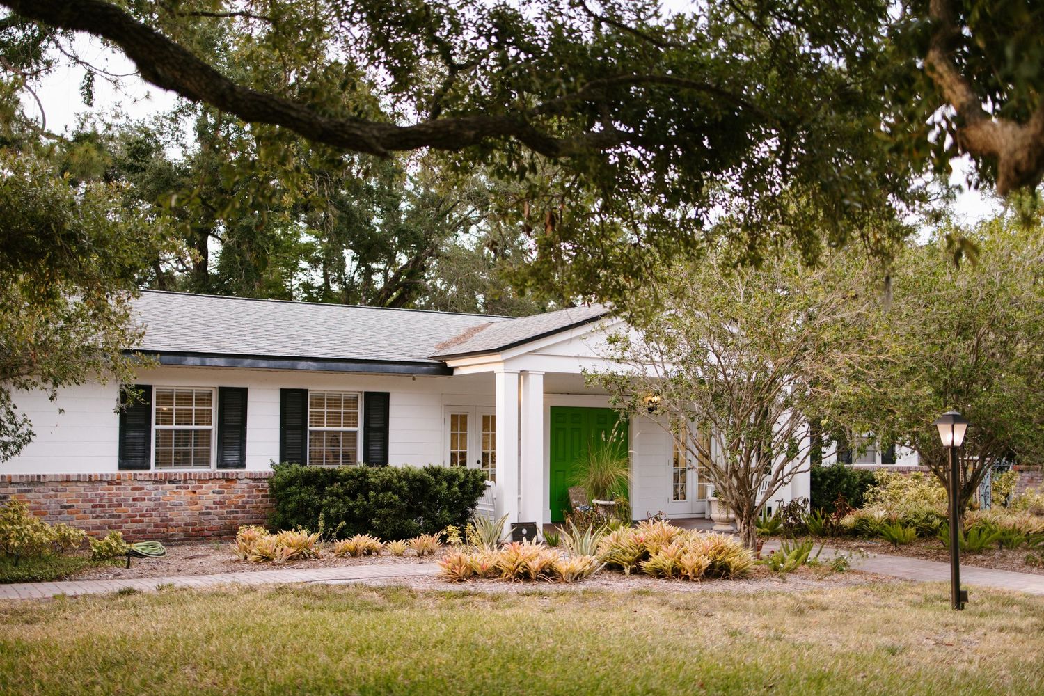 White ranch-style home with green front door surrounded by mature oak trees and landscaping.