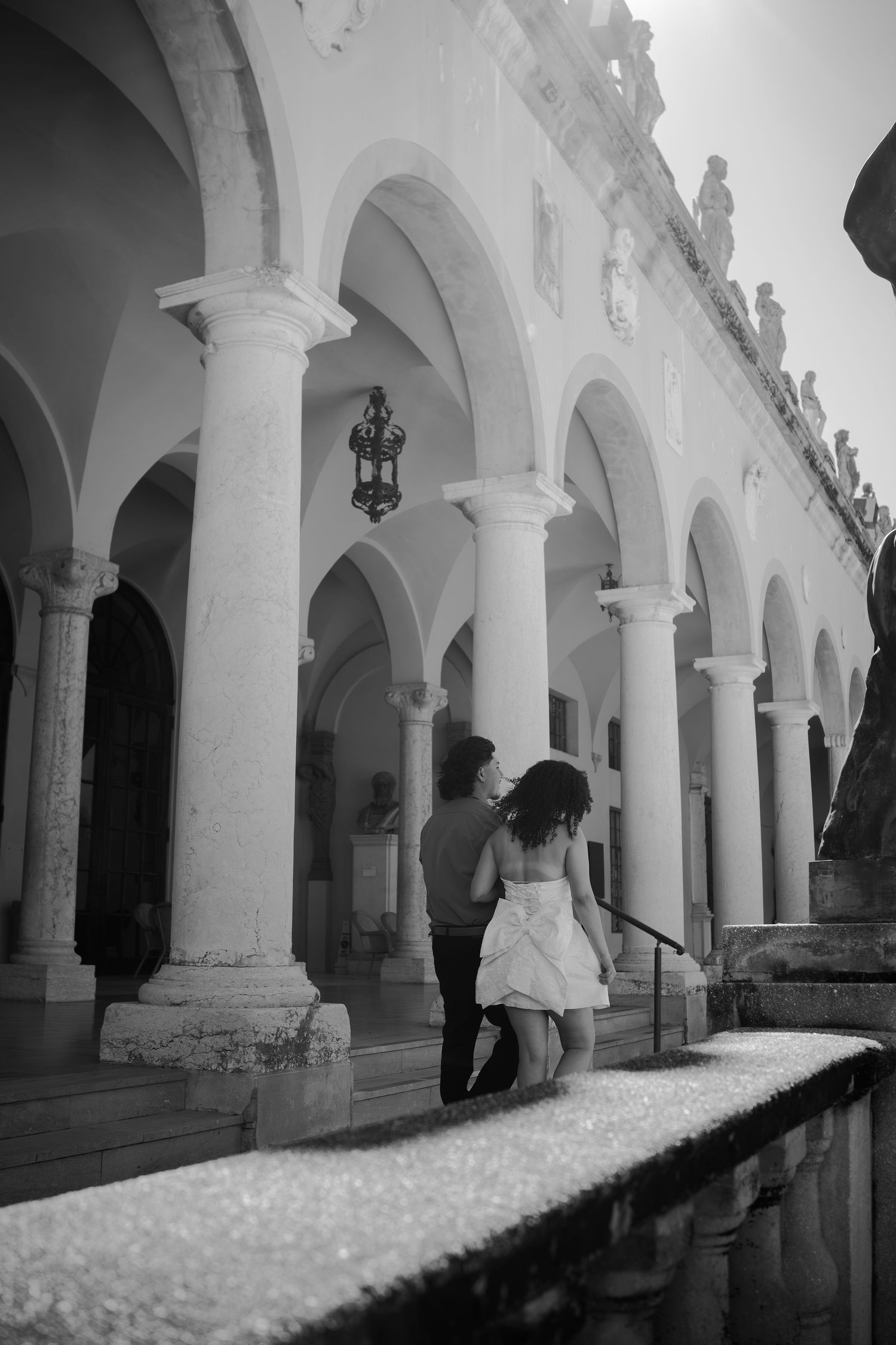 Black and white photo of couple climbing steps beneath arched colonnade of historic building.