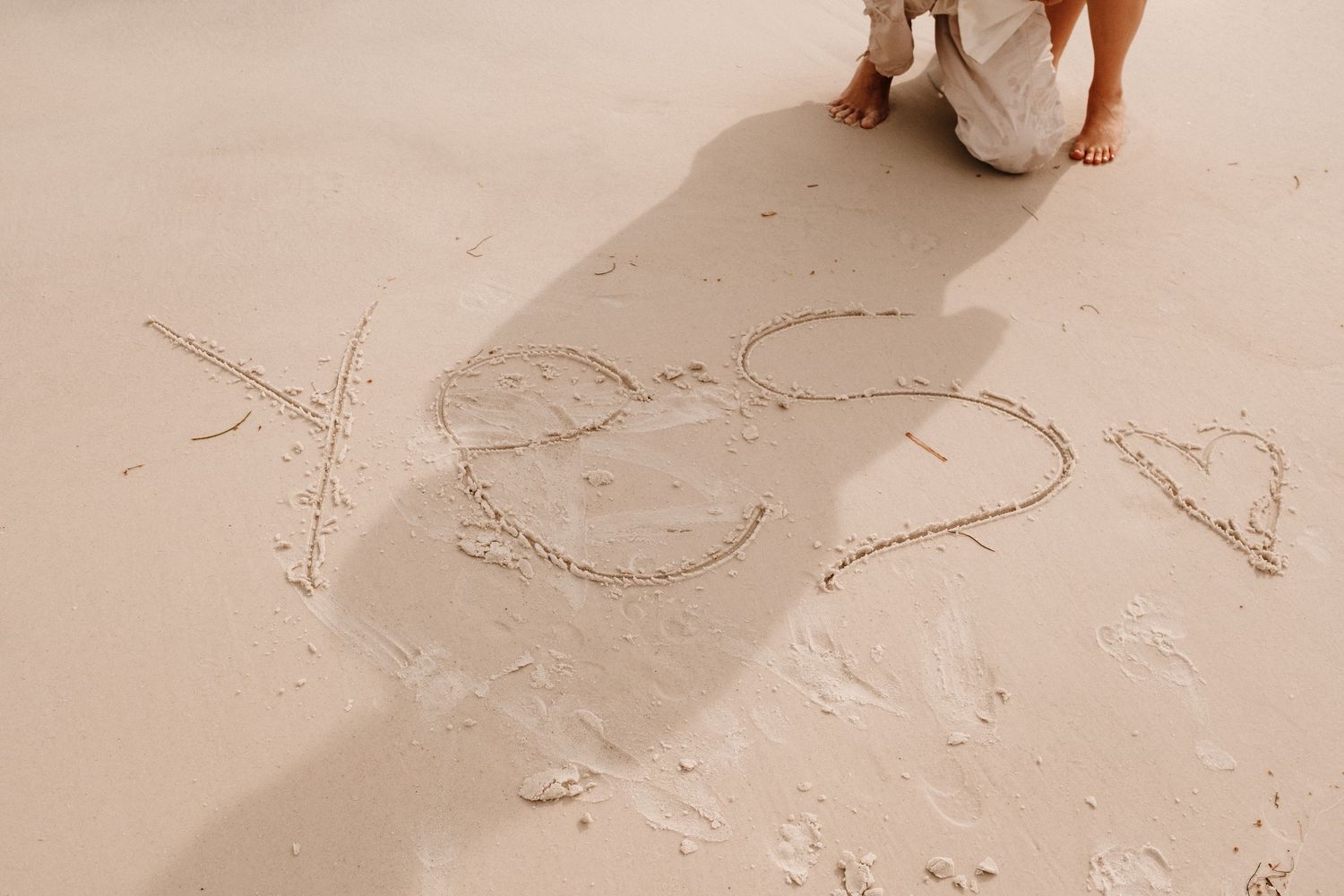 Person writing XOXO and hearts in sandy beach, romantic love message drawn in sand at seaside.