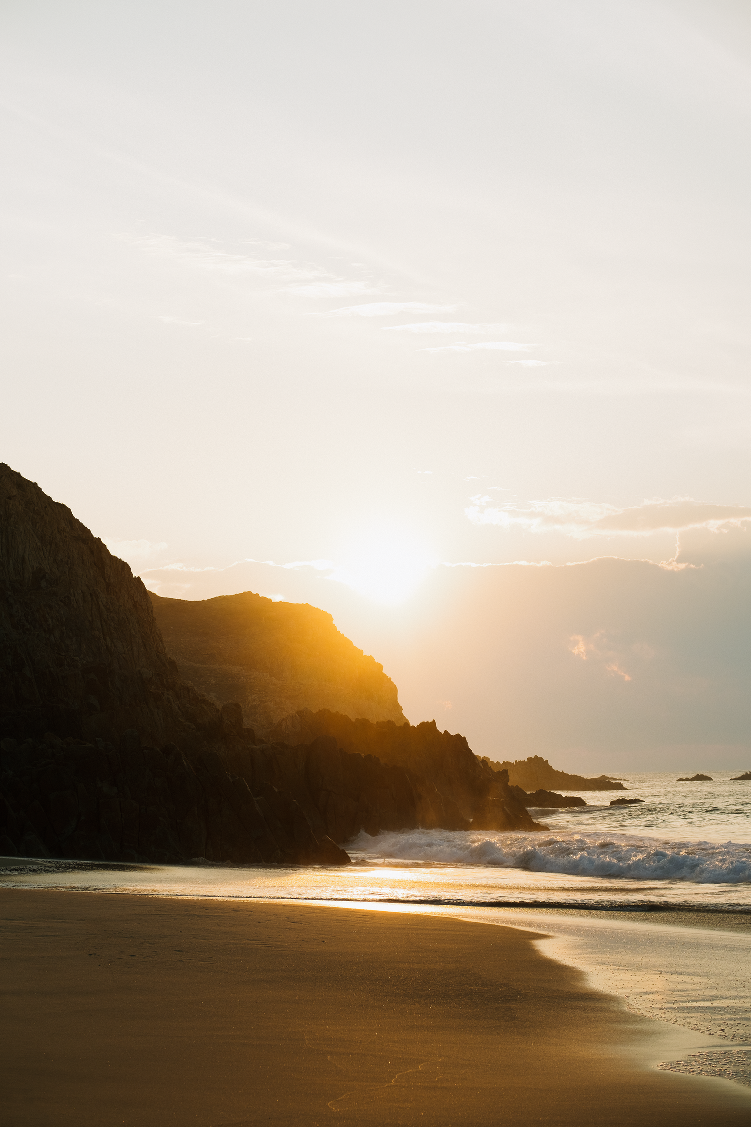 Warm sunset glow over coastal cliffs and sandy beach with ocean waves.